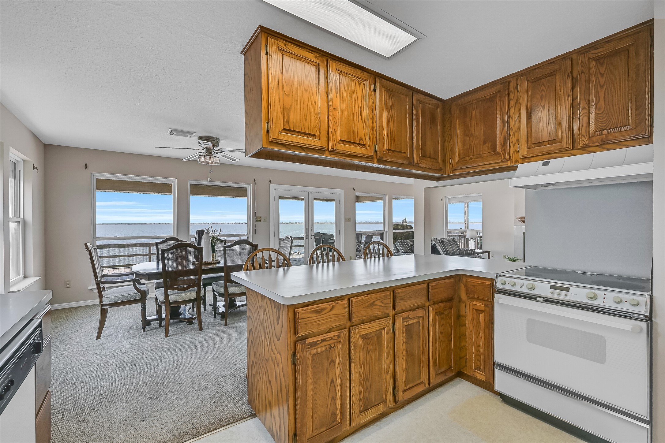 A large breakfast bar provides additional seating and serves as a natural gathering spot for guests. Oak cabinetry, plentiful storage, white appliances, and a walk-in pantry create a practical workspace designed for easy coastal living.