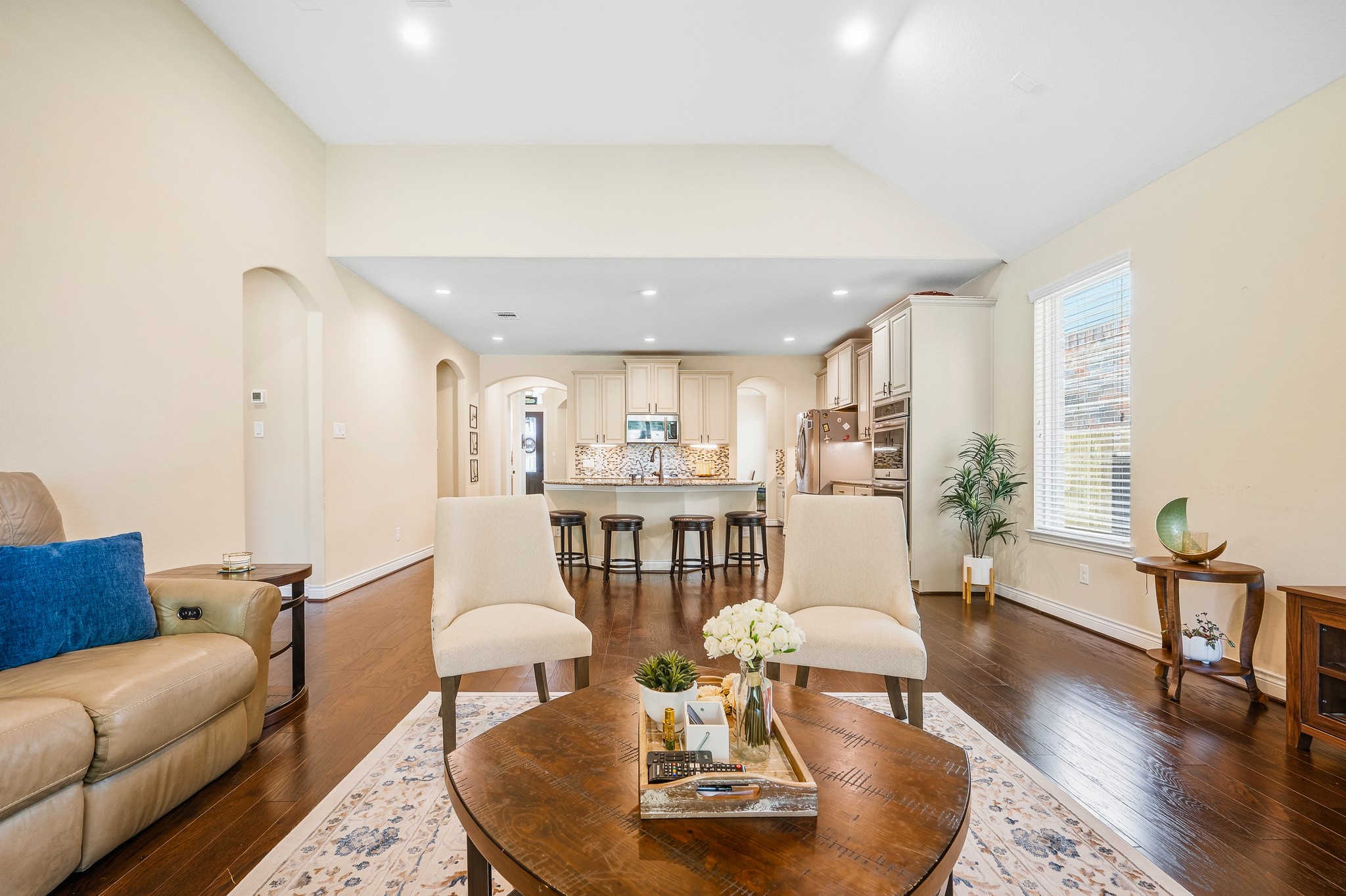 Experience the perfect blend of elegance and functionality in this spacious open-concept living area, featuring hardwood floors, a cozy seating arrangement, and a modern kitchen with a large island and ample cabinetry, ideal for entertaining and everyday living.