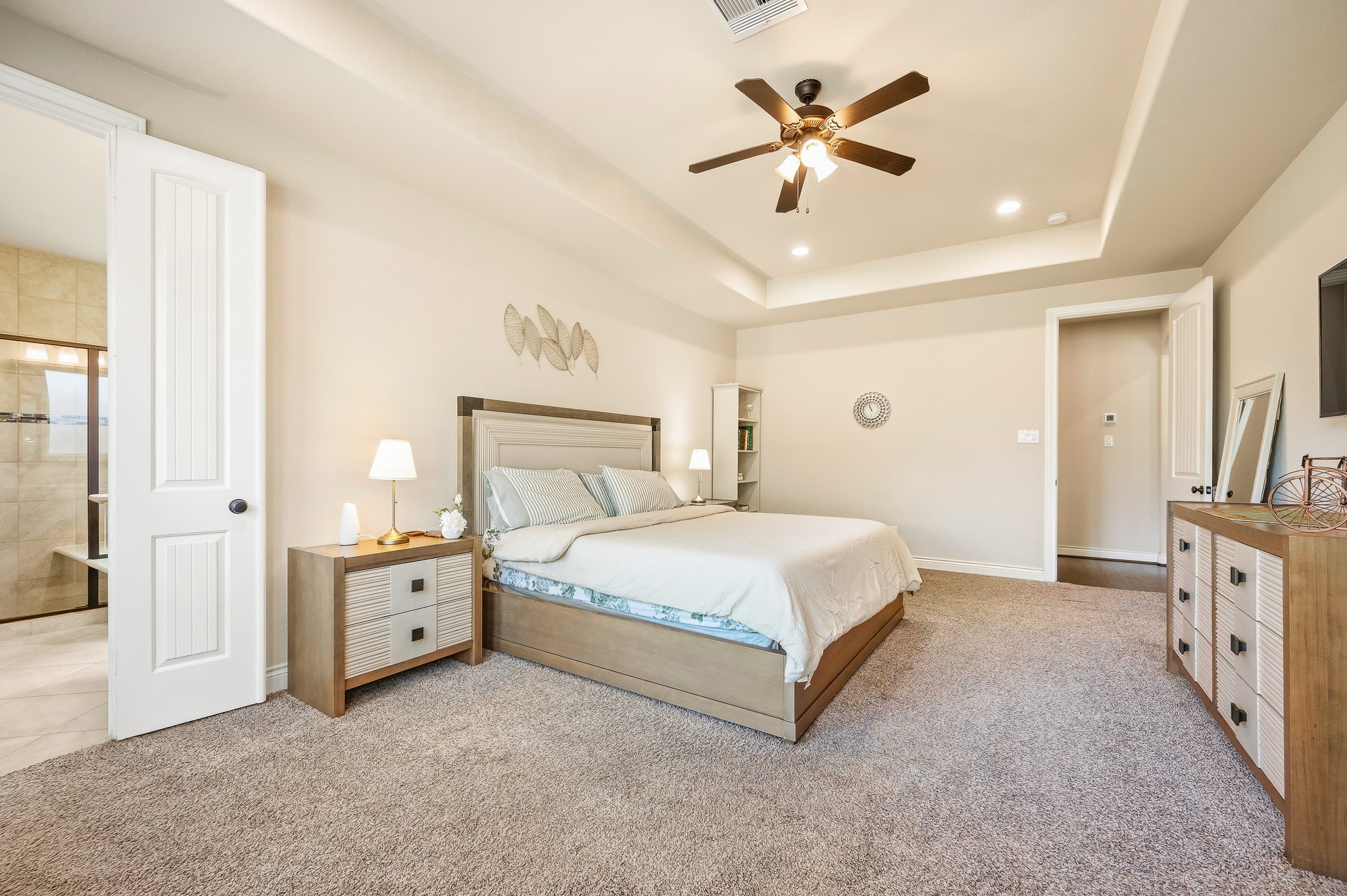 Indulge in comfort and style in this spacious bedroom with plush carpeting, a modern ceiling fan, abundant natural light, and a chic en-suite bathroom.