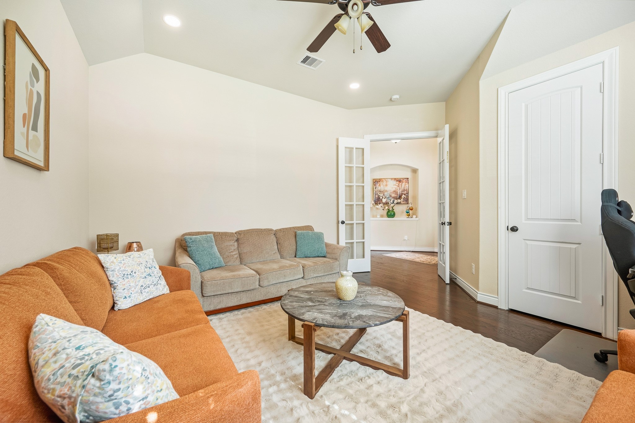Embrace the charm of a cozy living area with warm-toned sofas and a central round coffee table, effortlessly flowing into a bright hallway through elegant French doors.