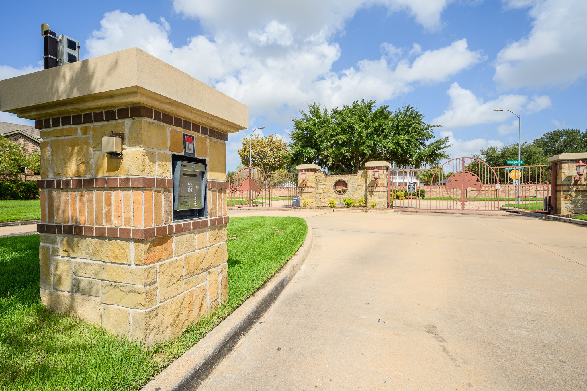 Discover elegant privacy at this gated community entrance, featuring secure keypad access, lush landscaping, and stately stone pillars.