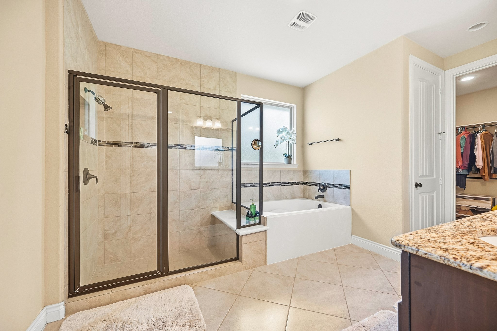 Experience luxury in this elegant bathroom featuring a spacious glass-enclosed shower, a relaxing bathtub with stylish tiled surround, and the convenience of an adjoining walk-in closet.