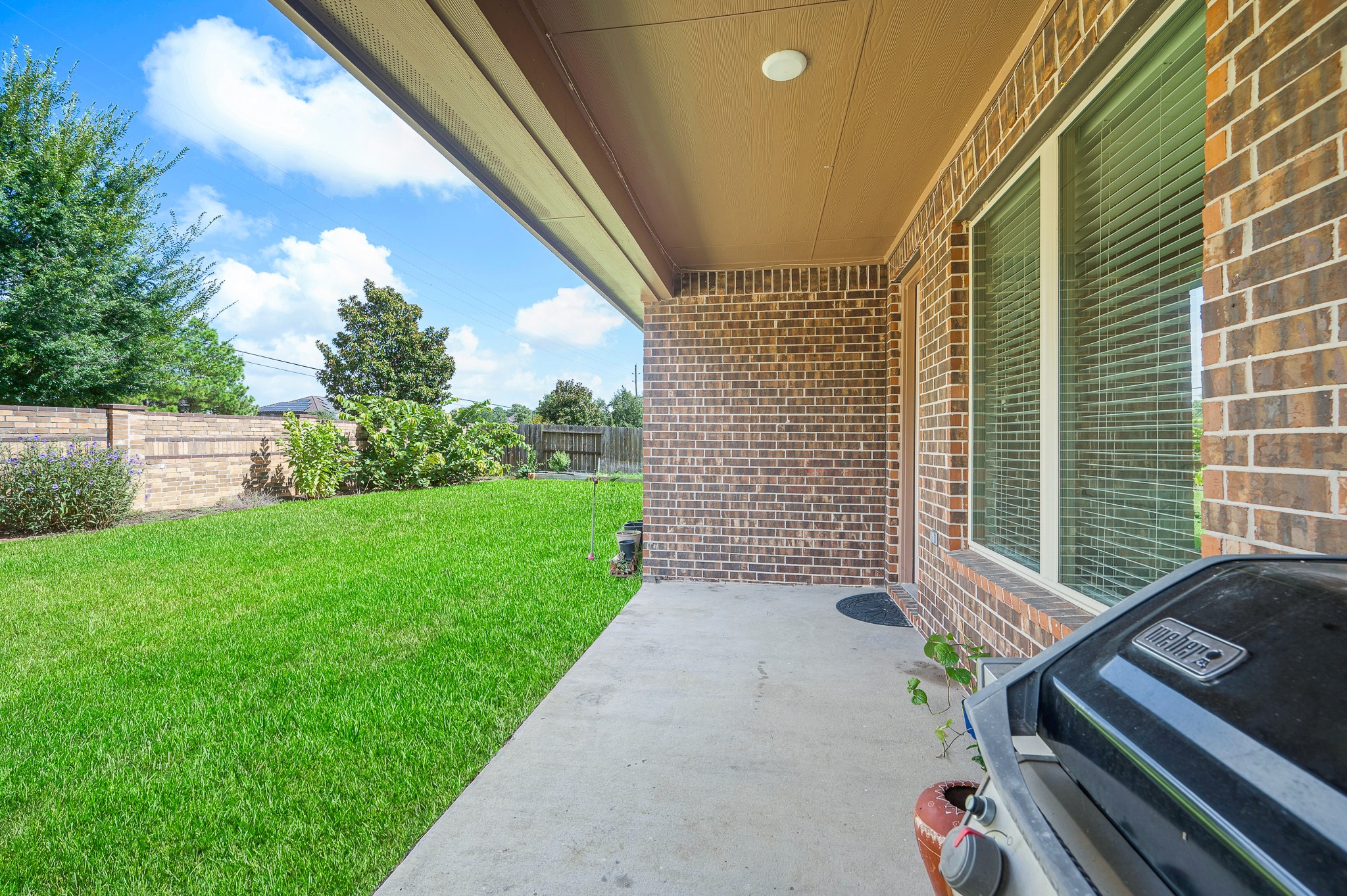 A charming covered patio with elegant brick accents overlooks a lush, well-maintained backyard, perfect for outdoor gatherings and relaxation.