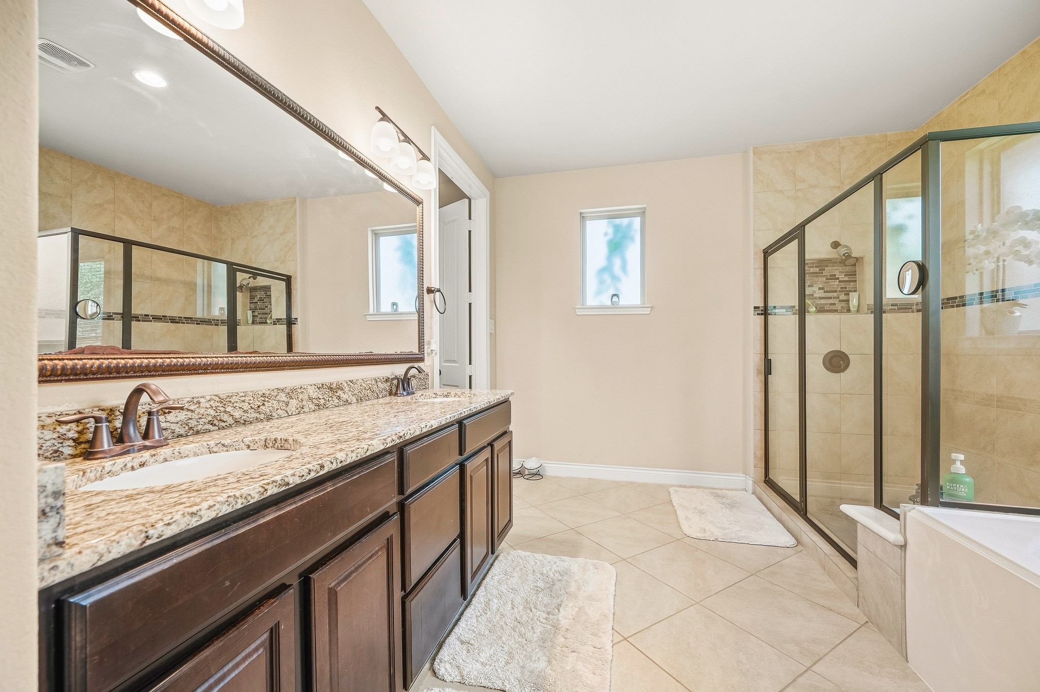 Experience elegance in this luxurious bathroom featuring a spacious double vanity with granite countertops, a large glass-enclosed shower, and neutral tile flooring for a sophisticated touch.