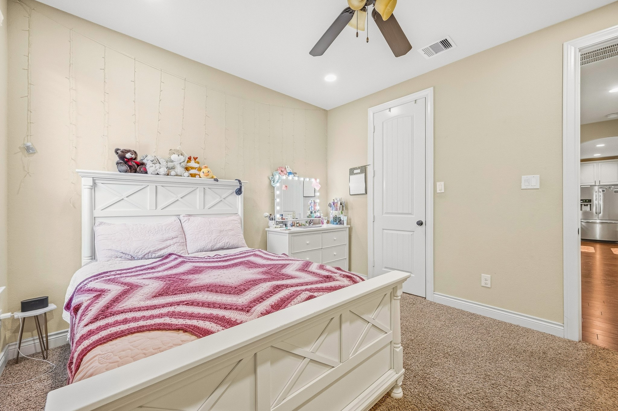 A cozy bedroom featuring a white bedframe, plush carpeting, and soft lighting offers a warm, inviting atmosphere perfect for relaxation.