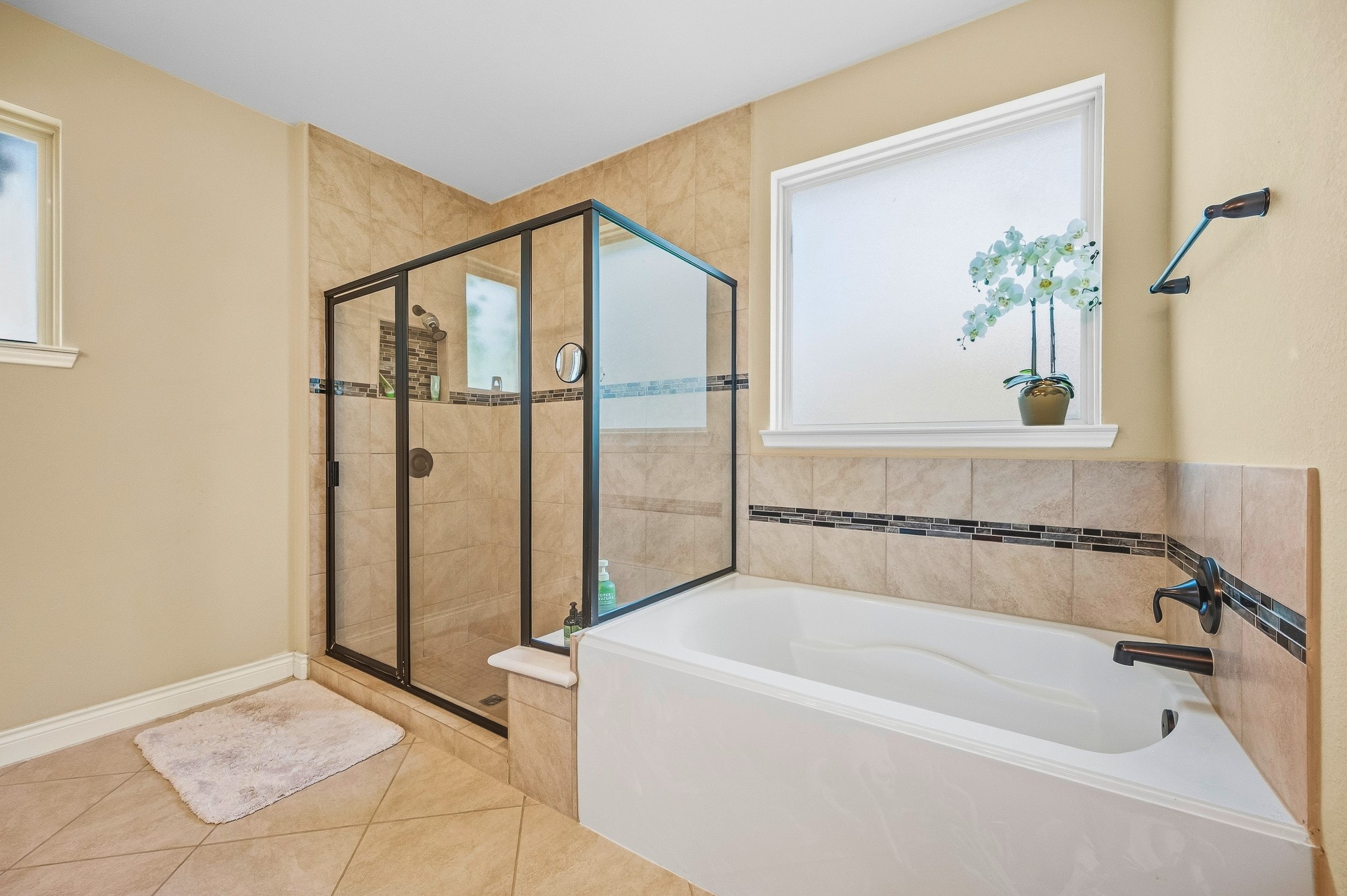 Experience the elegance of a bathroom with a spacious glass-enclosed shower and relaxing bathtub, adorned with stylish tile accents and bathed in abundant natural light.