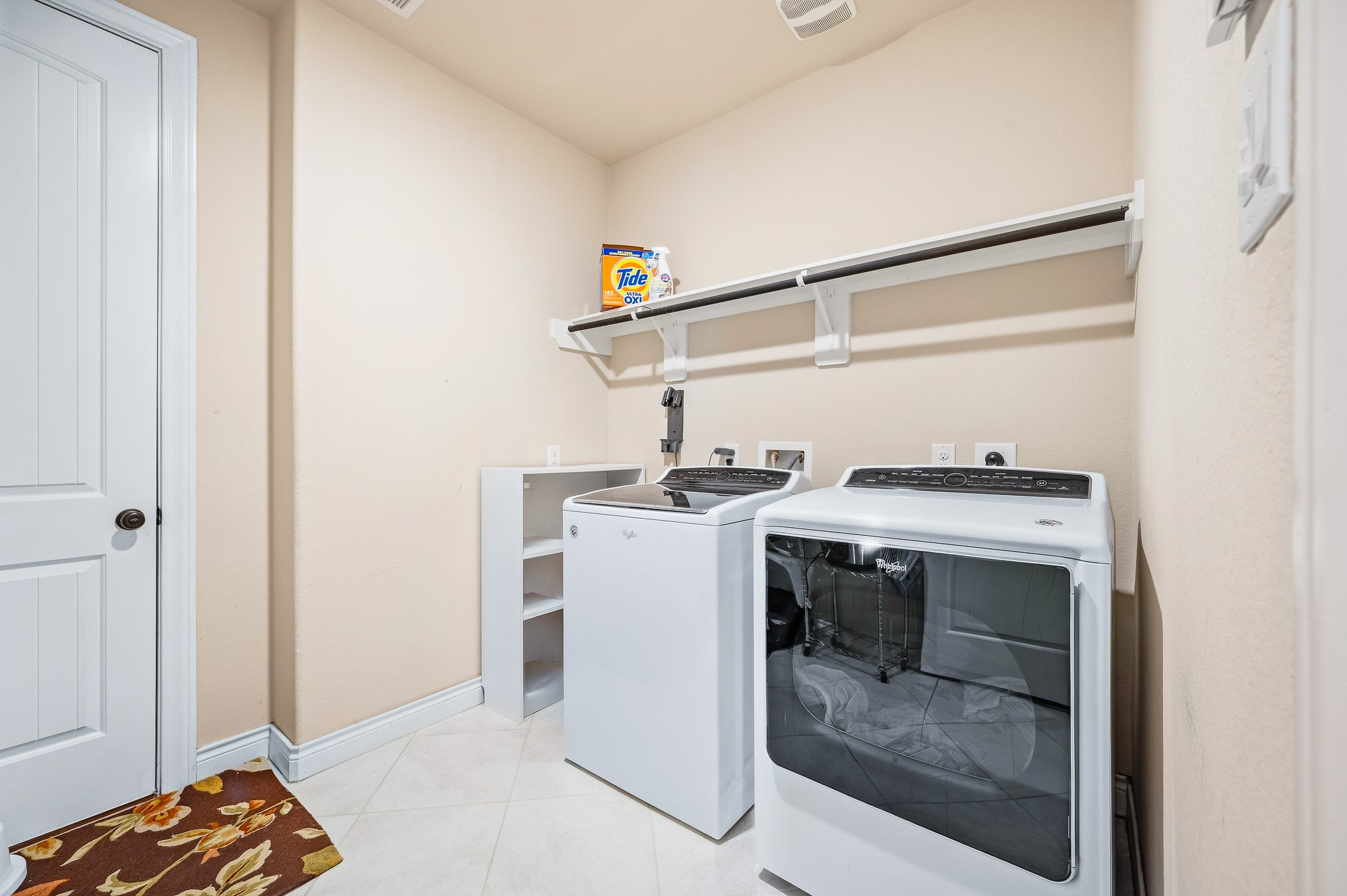 Discover a modern laundry room featuring a sleek washer and dryer set, abundant shelving for organized storage, and easy-to-maintain neutral tile flooring.