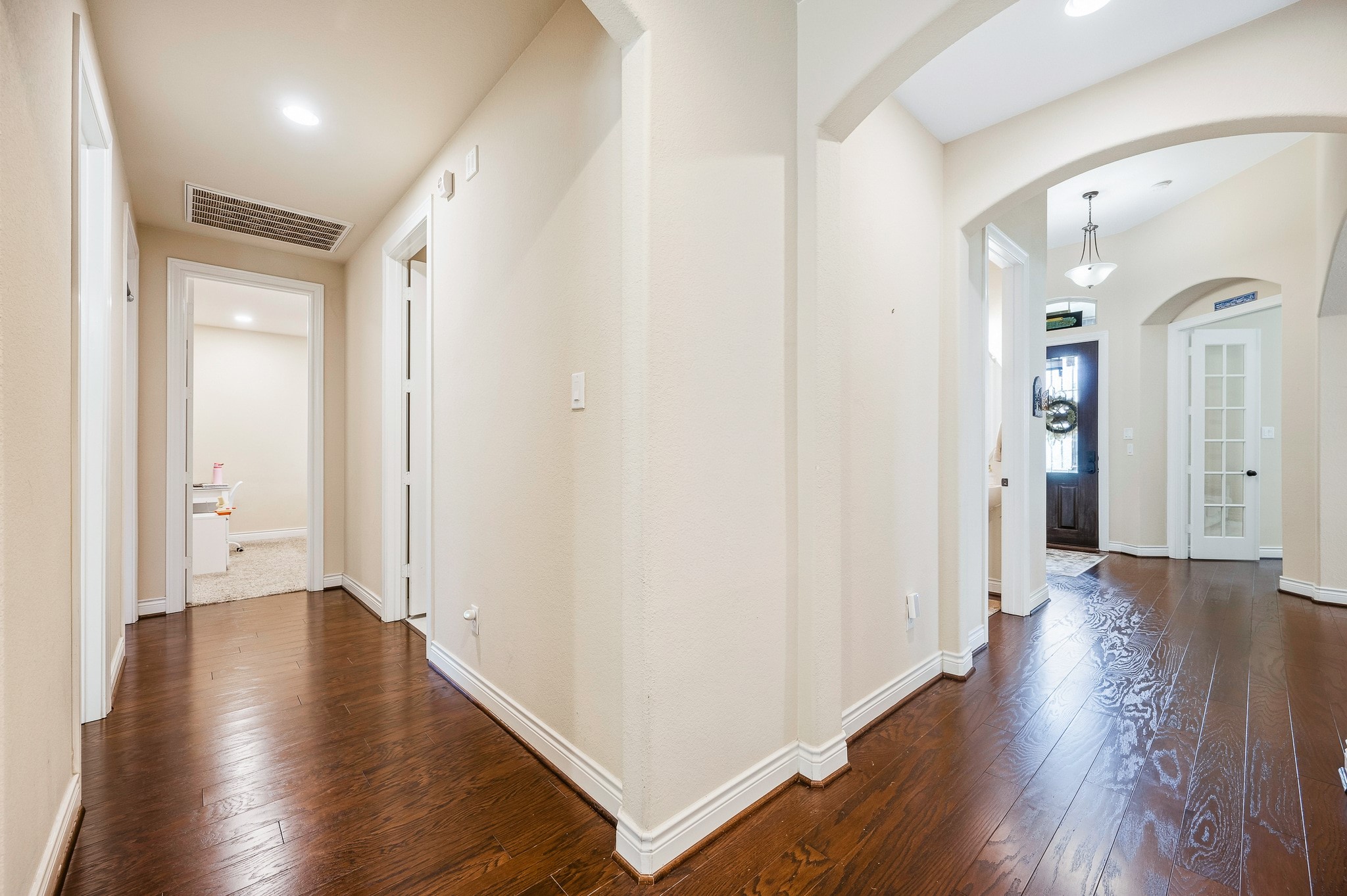 An elegant hallway with rich wood flooring, soft lighting, and arched doorways warmly invites you into spacious rooms, creating an inviting atmosphere.