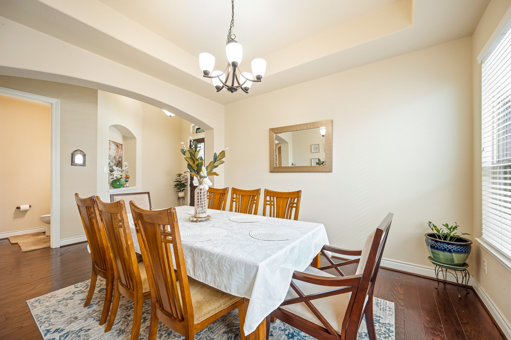 Elegant dining room featuring a stylish chandelier, warm wood flooring, and ample natural light from large windows, perfect for hosting gatherings.