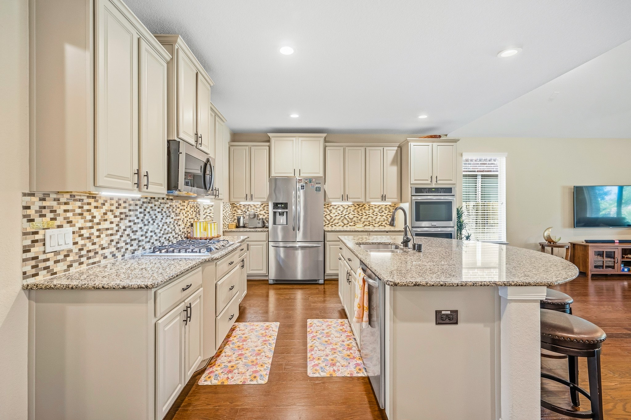 Experience a chef's dream kitchen with elegant granite countertops, a spacious island with seating, stainless steel appliances, and a chic mosaic tile backsplash, perfect for culinary enthusiasts.