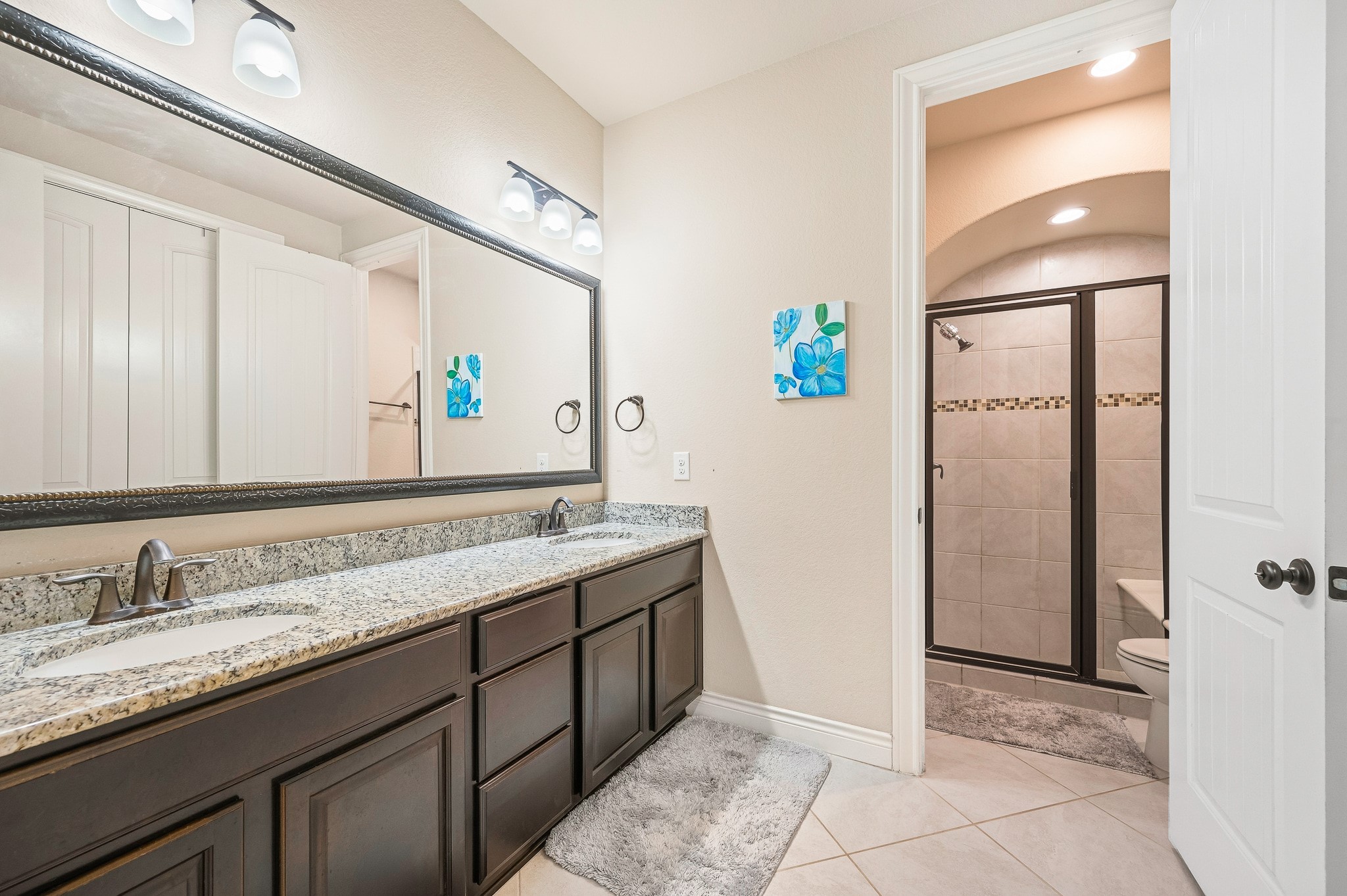 Experience elegance in this bathroom with a spacious dual-sink vanity topped with granite, a large framed mirror, and a walk-in shower featuring stylish tile detailing.