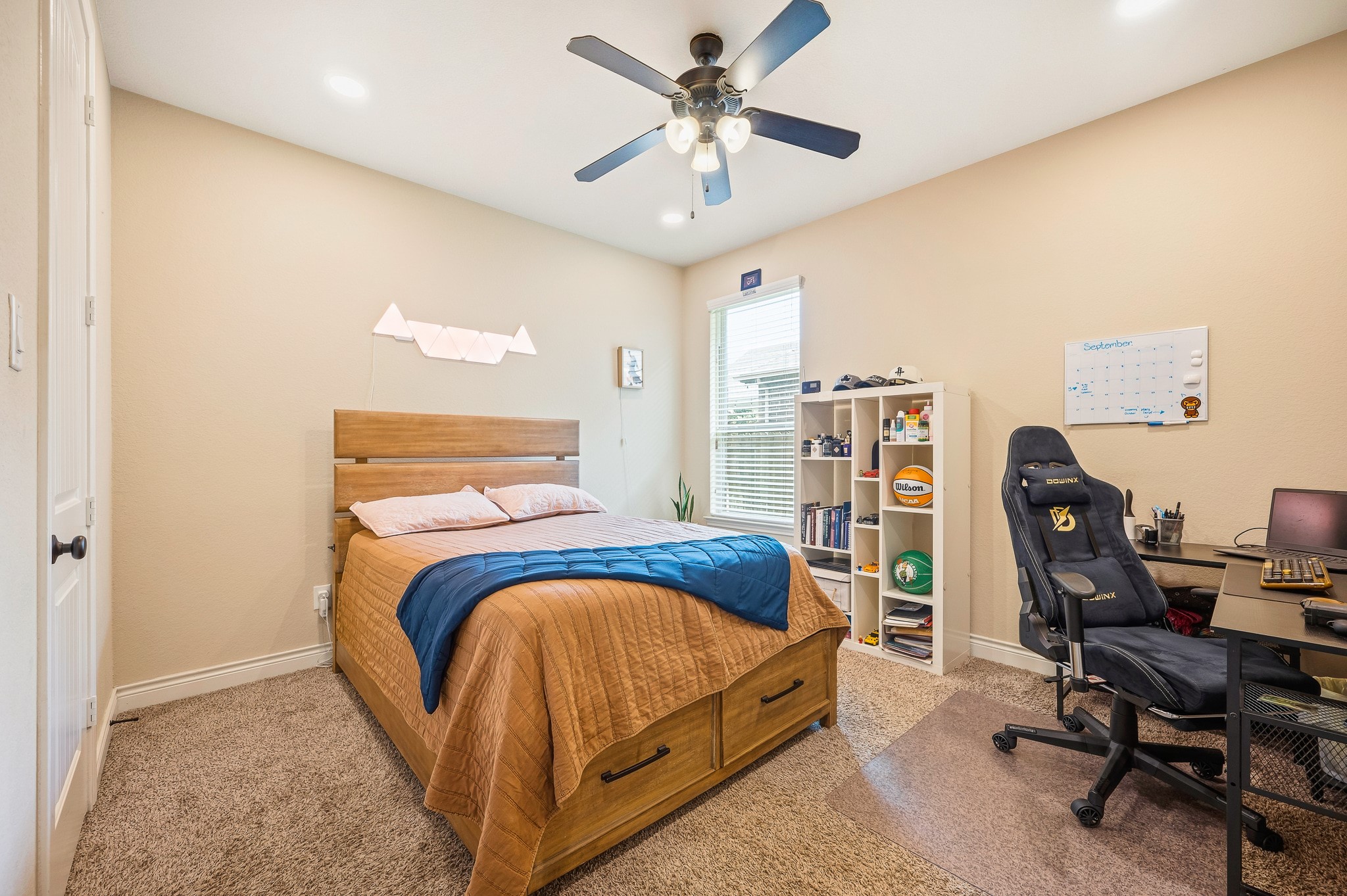 Cozy bedroom featuring a comfortable bed with under-storage, a ceiling fan, and a well-organized desk area perfect for work or study.