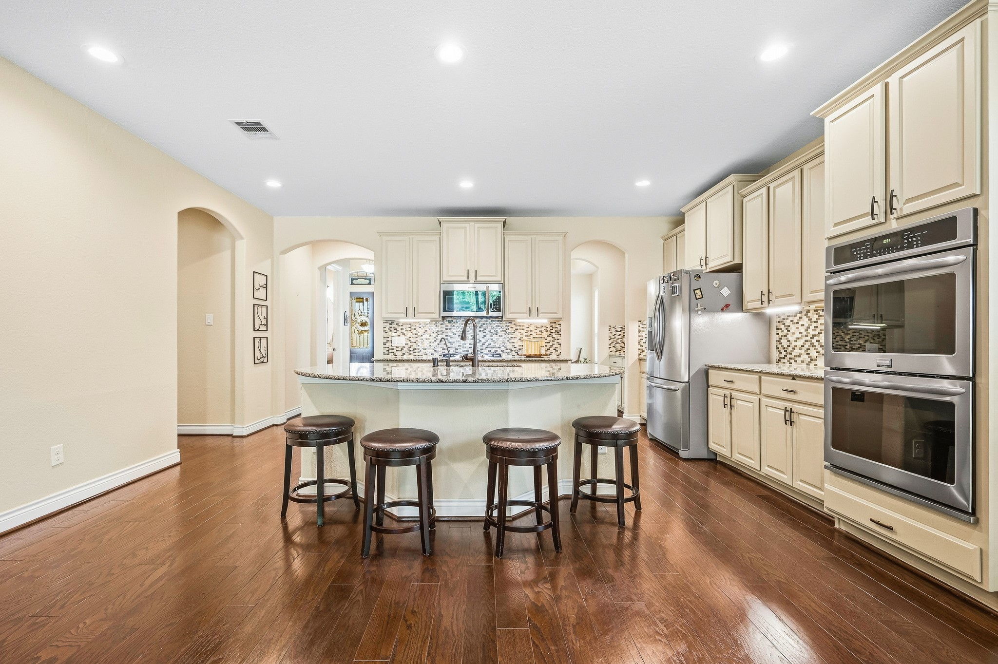 Experience culinary elegance in this spacious kitchen featuring exquisite cabinetry, a large center island with seating, modern stainless steel appliances, a stylish backsplash, and rich hardwood floors.