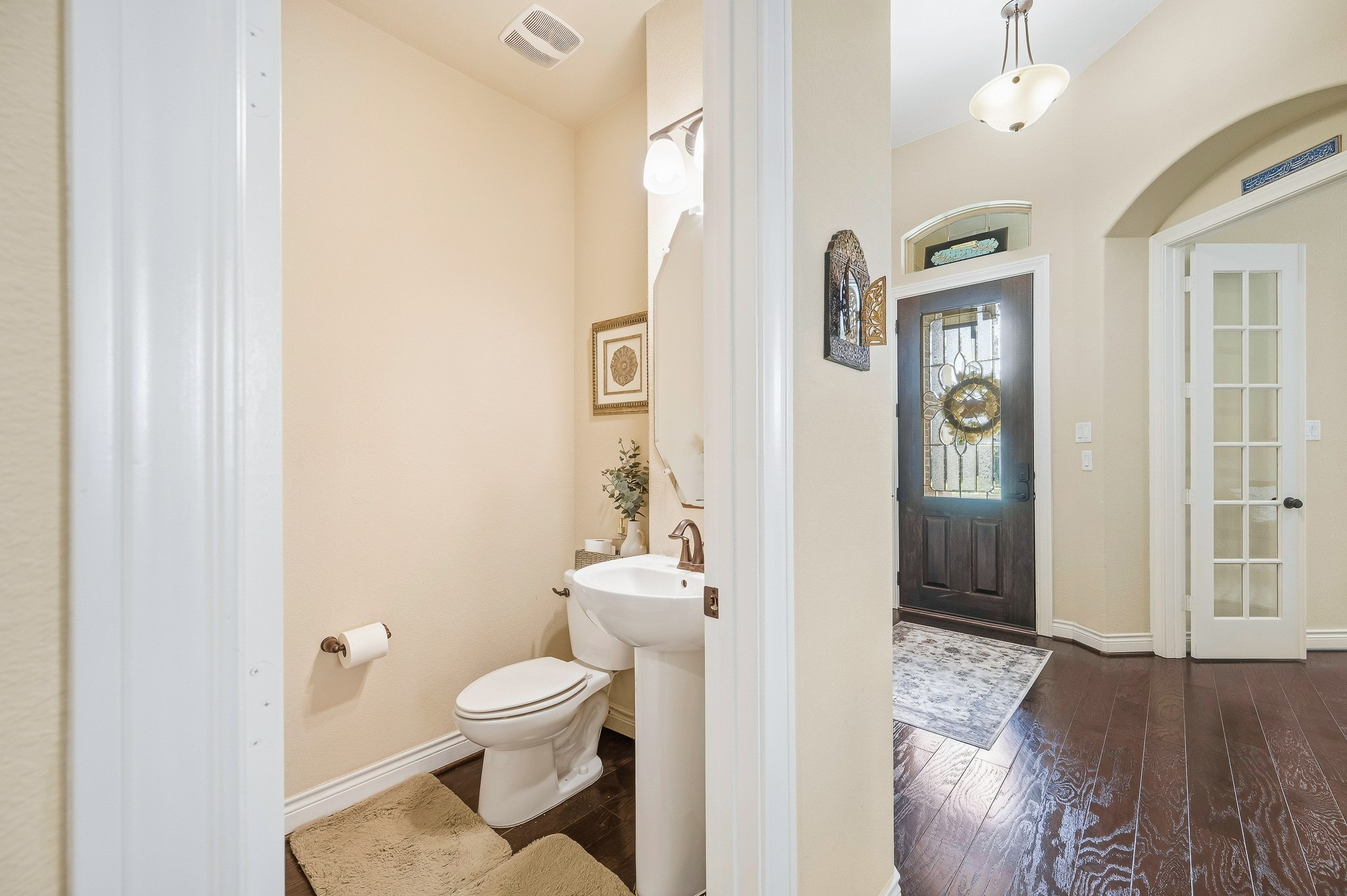 Charming entryway with elegant dark wood flooring and a welcoming glass-paneled door leads seamlessly to a cozy powder room featuring modern fixtures and warm lighting.