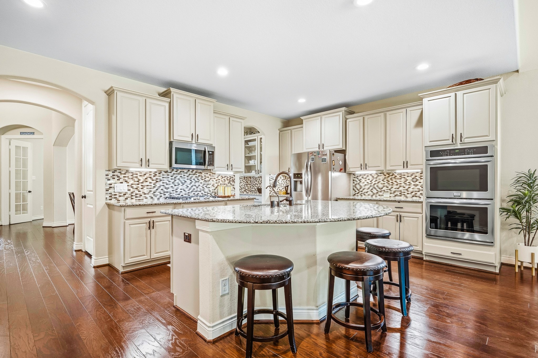 Experience culinary luxury in a spacious gourmet kitchen featuring elegant cabinetry, granite countertops, a central island with seating, stainless steel appliances, and a stylish mosaic backsplash.