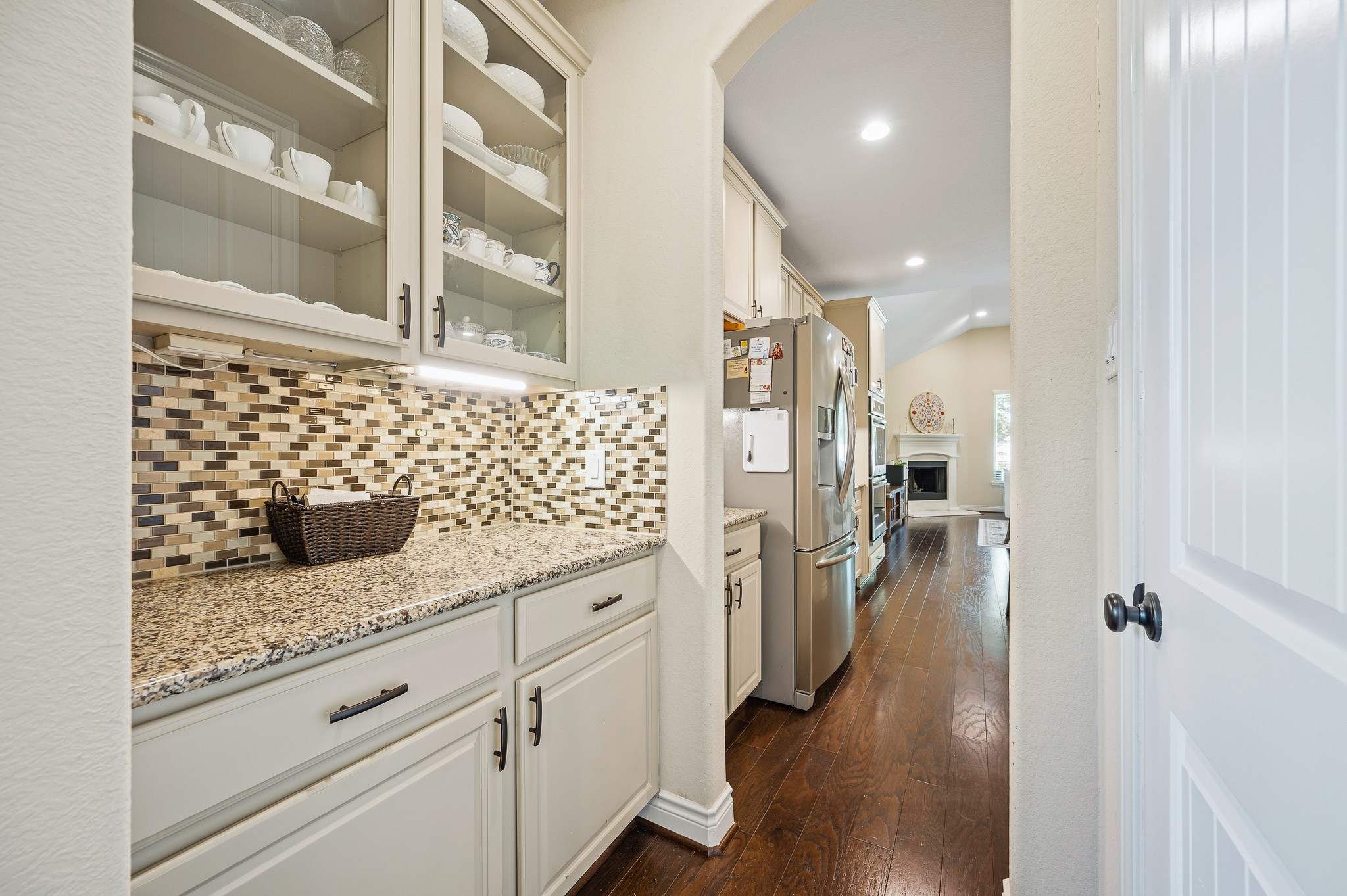 Experience the elegance of a charming butler's pantry with sleek granite countertops and refined cabinetry, seamlessly flowing into a spacious kitchen adorned with stainless steel appliances and rich hardwood floors.