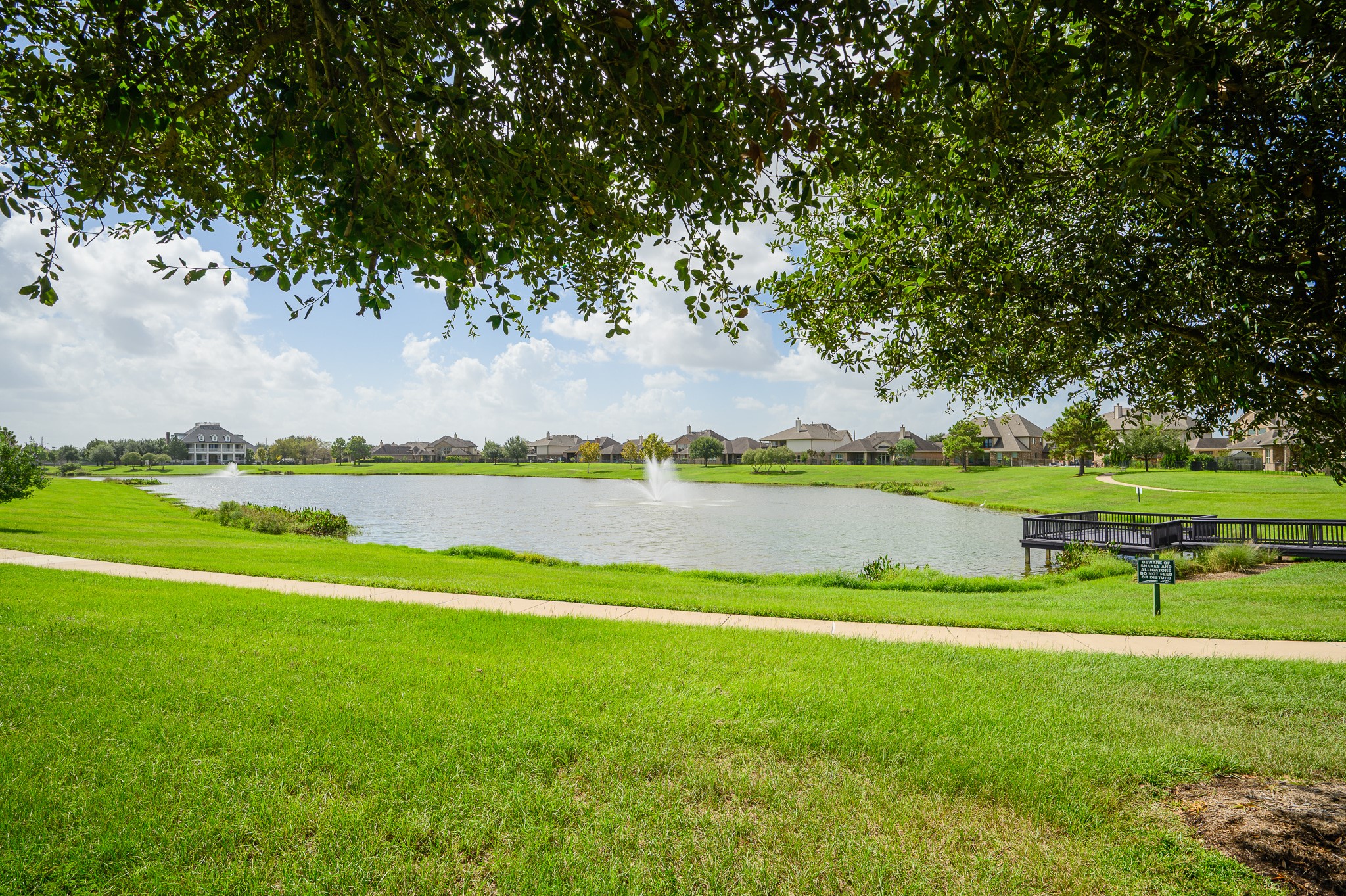 Embrace serene lakeside living with a picturesque fountain, lush greenery, and a charming bridge, ideal for leisurely strolls and peaceful relaxation.