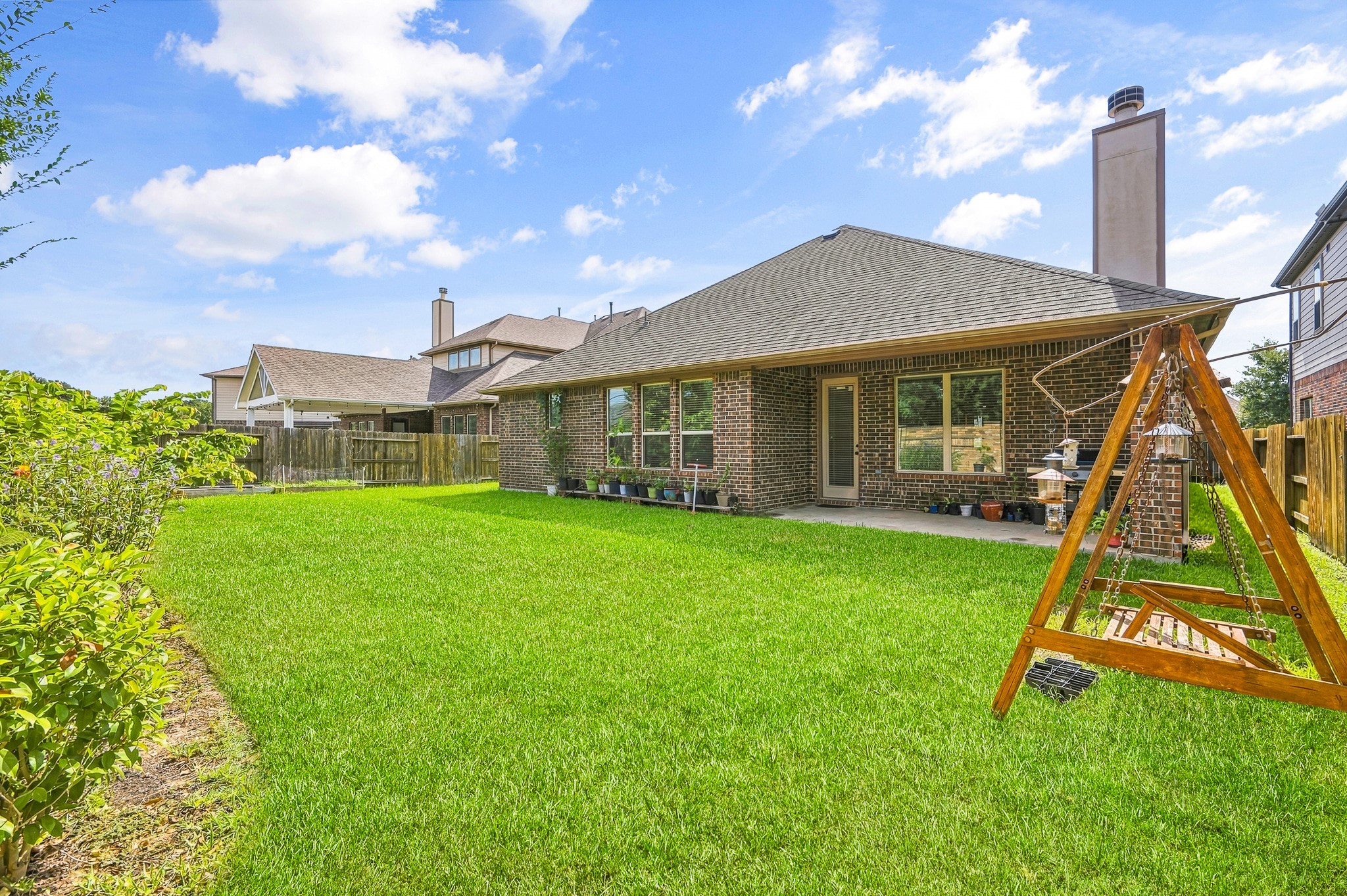 Discover a charming backyard oasis with a spacious lawn, cozy swing set, and a covered patio ideal for relaxation and entertainment.