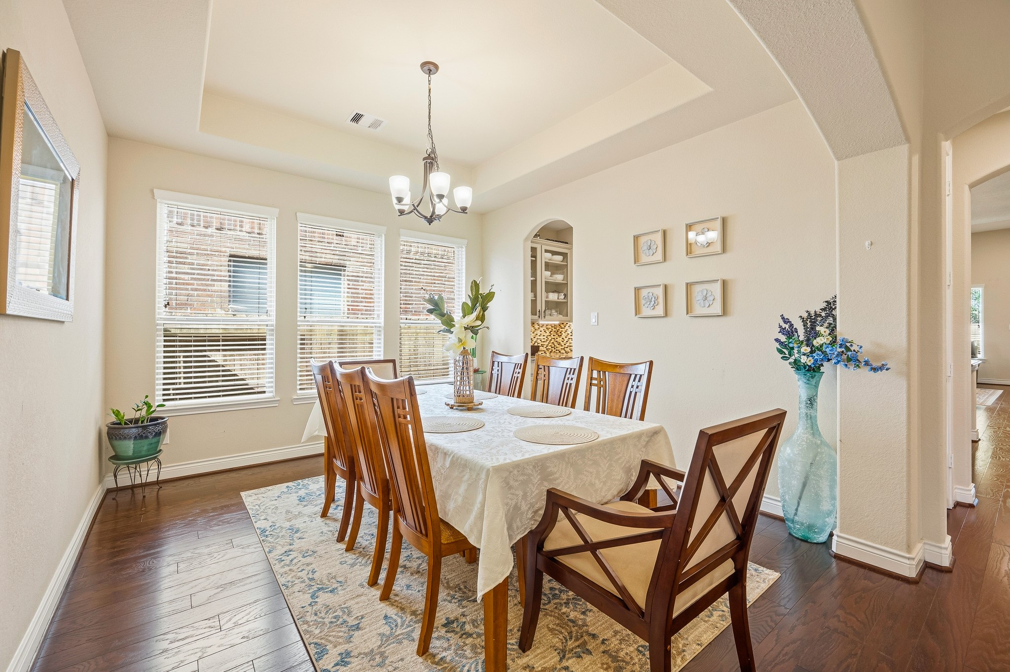 Elegant dining room with warm hardwood floors, abundant natural light from large windows, and a stylish chandelier above a spacious table, perfect for gatherings.