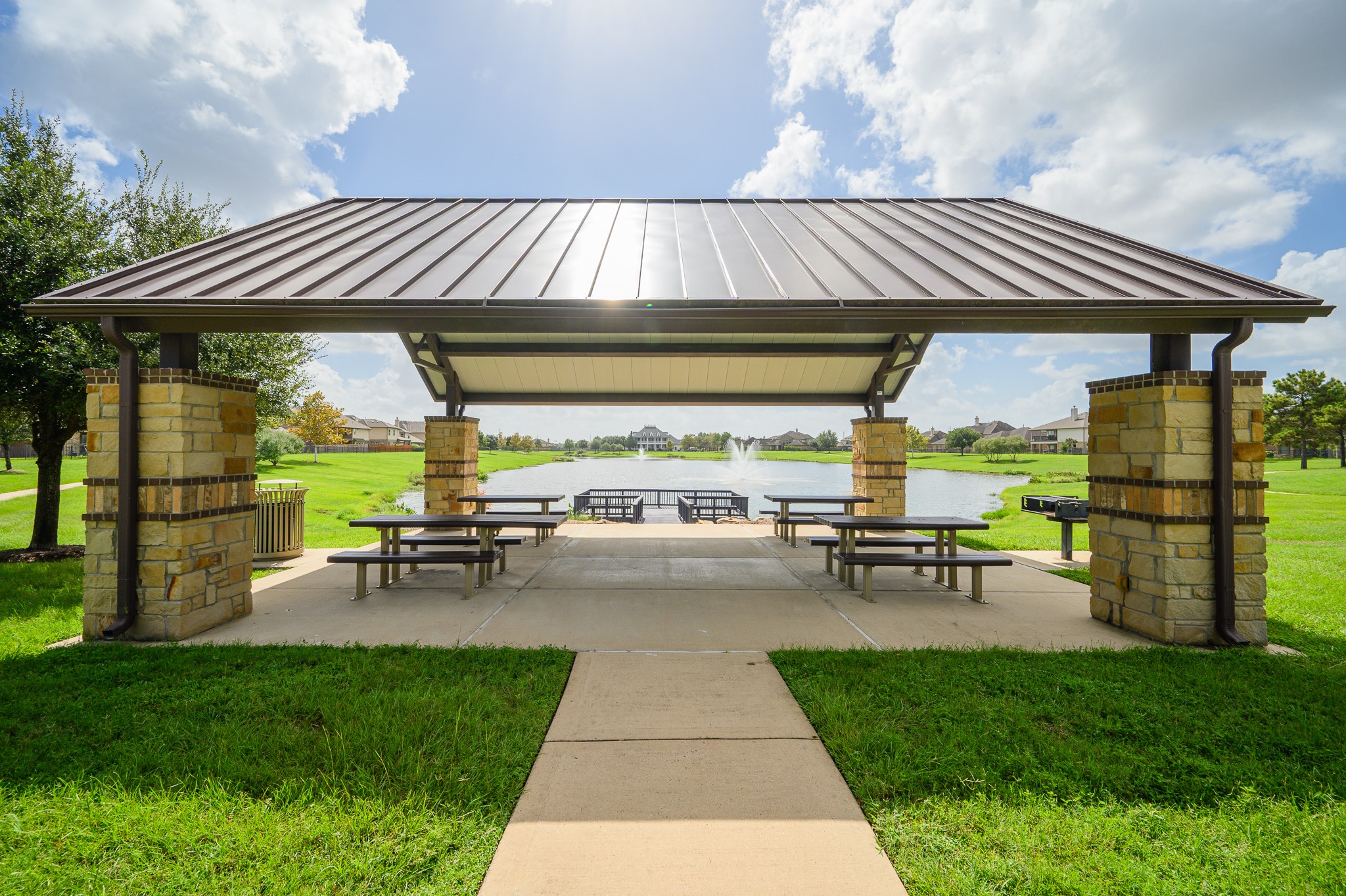 Experience the perfect setting for outdoor gatherings at this charming pavilion with picnic tables and grills, all while overlooking a serene pond adorned with a graceful fountain.