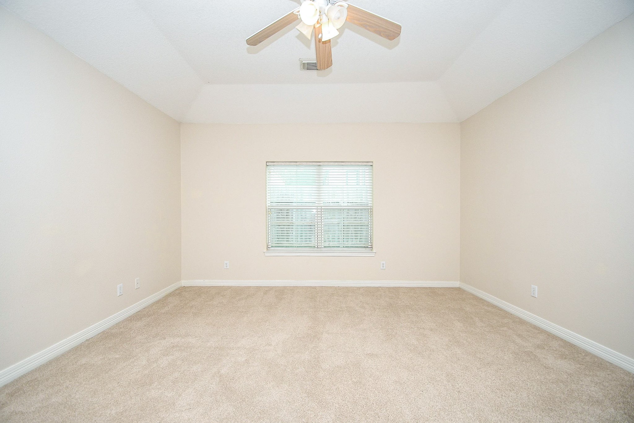 This bright, spacious room features neutral walls, plush carpet, a central window with blinds, and a ceiling fan, offering a cozy and versatile space.