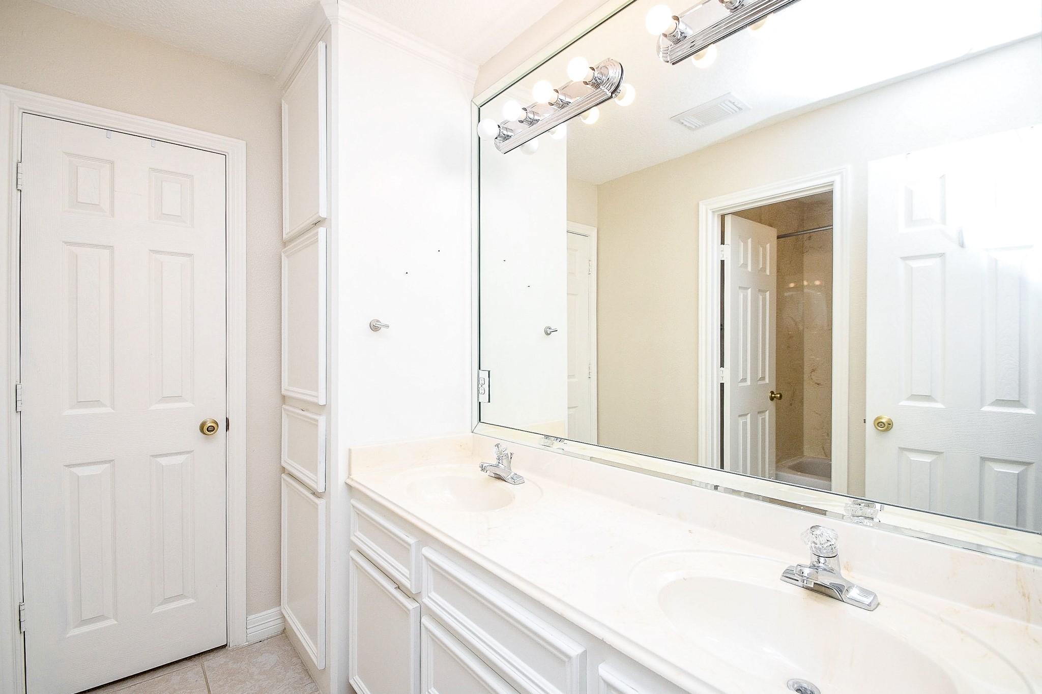 This bathroom features a large mirror above a dual-sink vanity with bright lighting. It has clean, white cabinetry, and a neutral color palette, providing a fresh and spacious feel.