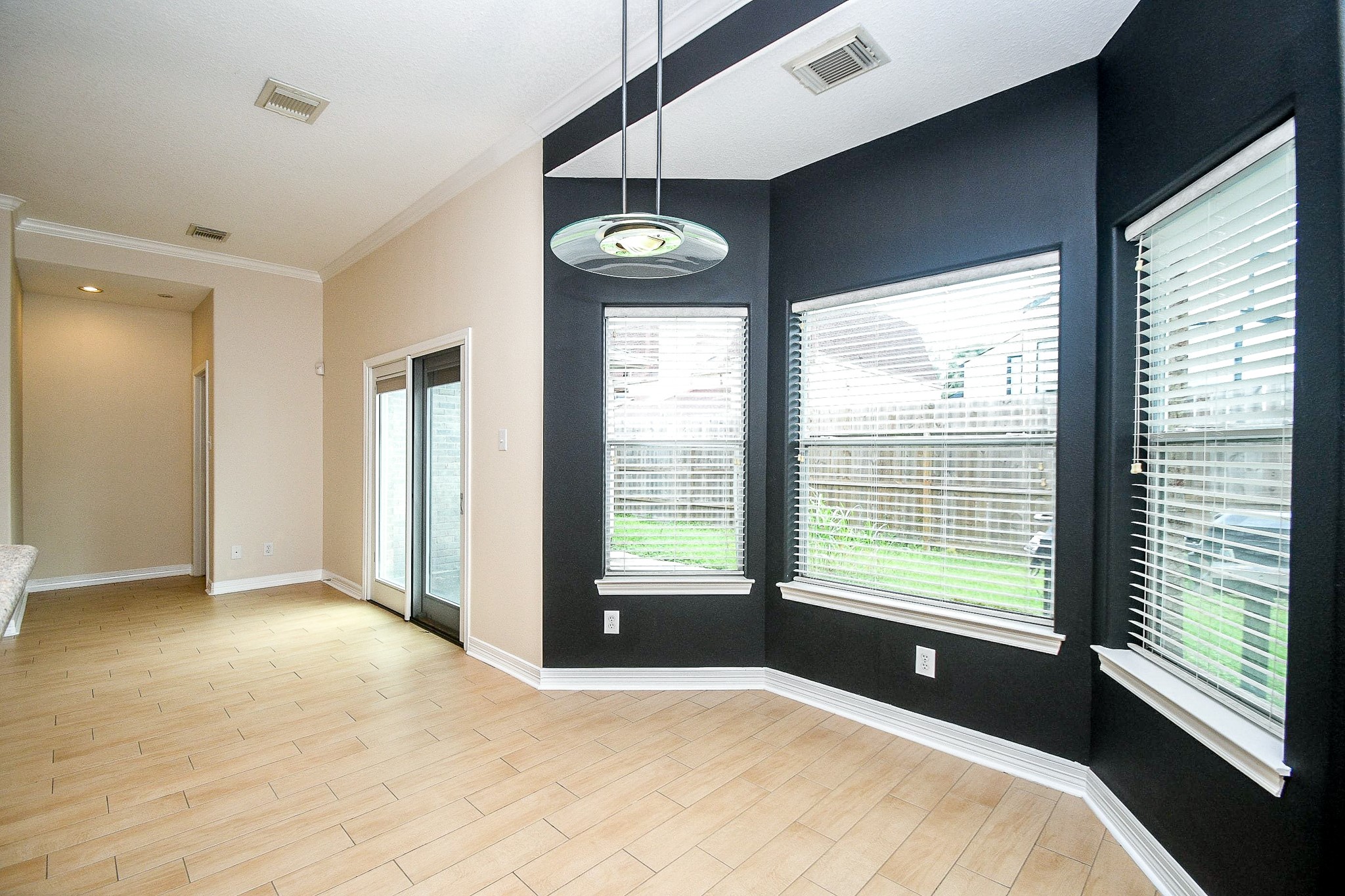 Bright dining area with large windows, modern light fixture, and wood-look tile flooring. The room opens to a hallway and features double glass doors leading outside.
