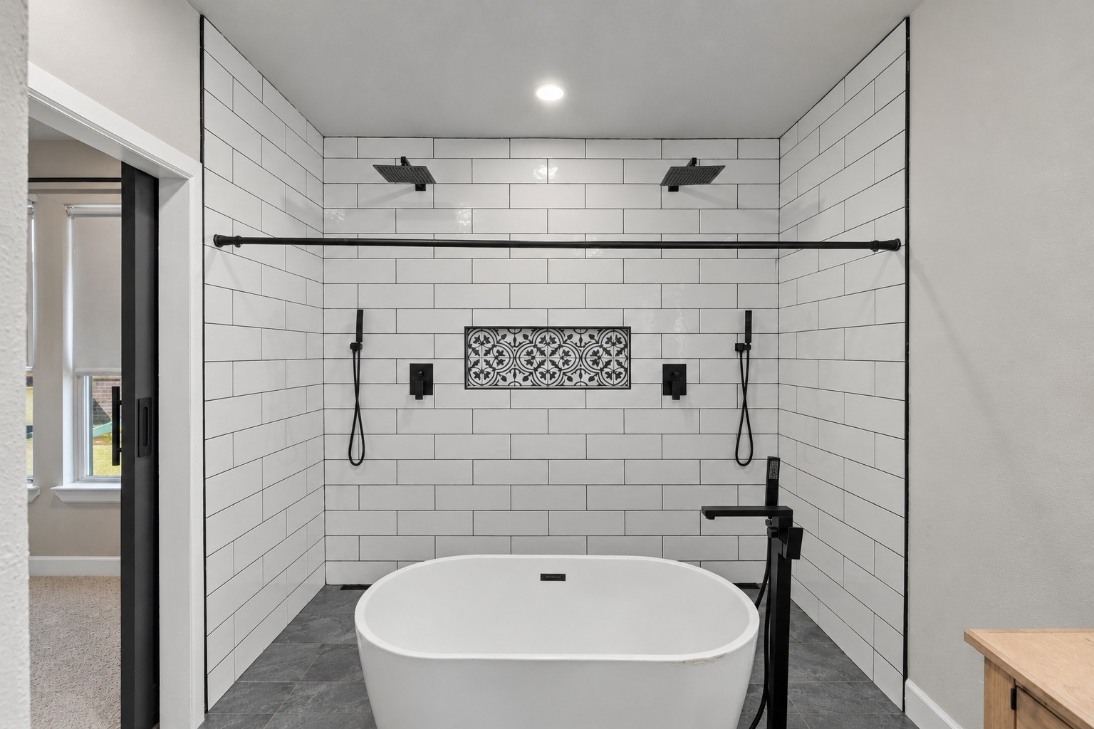 Spa-inspired wet room featuring a freestanding soaking tub, dual rainfall showers, and decorative tile accents.