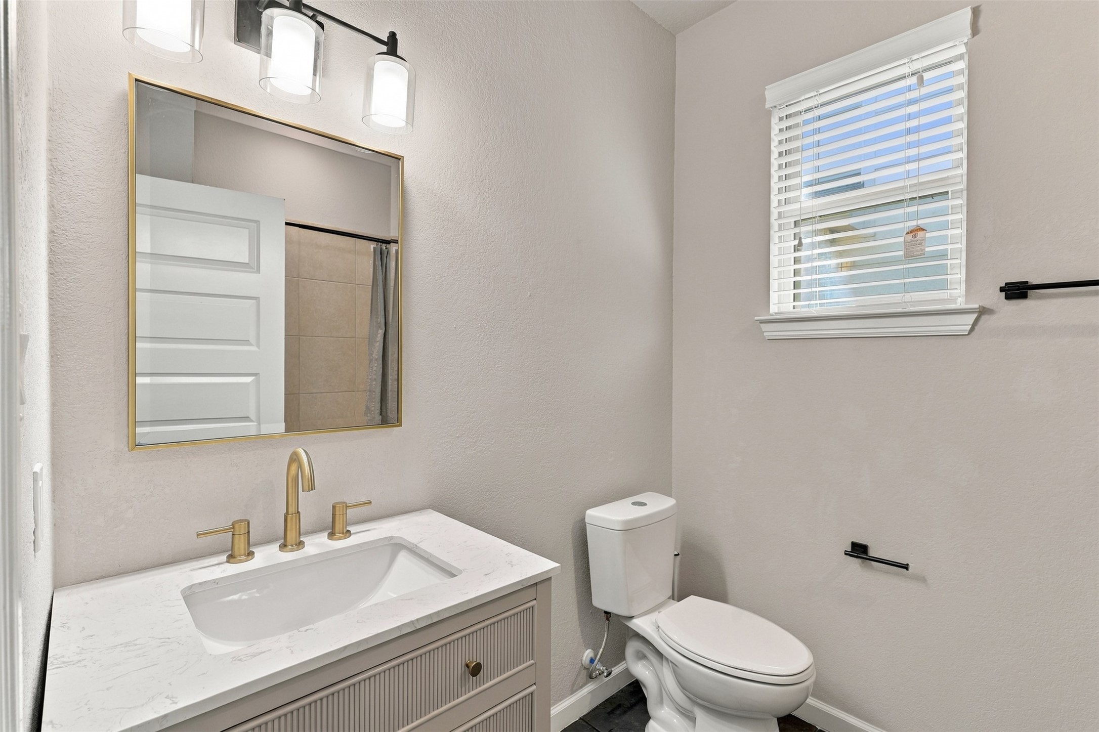 Secondary bathroom featuring a modern vanity, gold-tone fixtures, and a window for natural light.