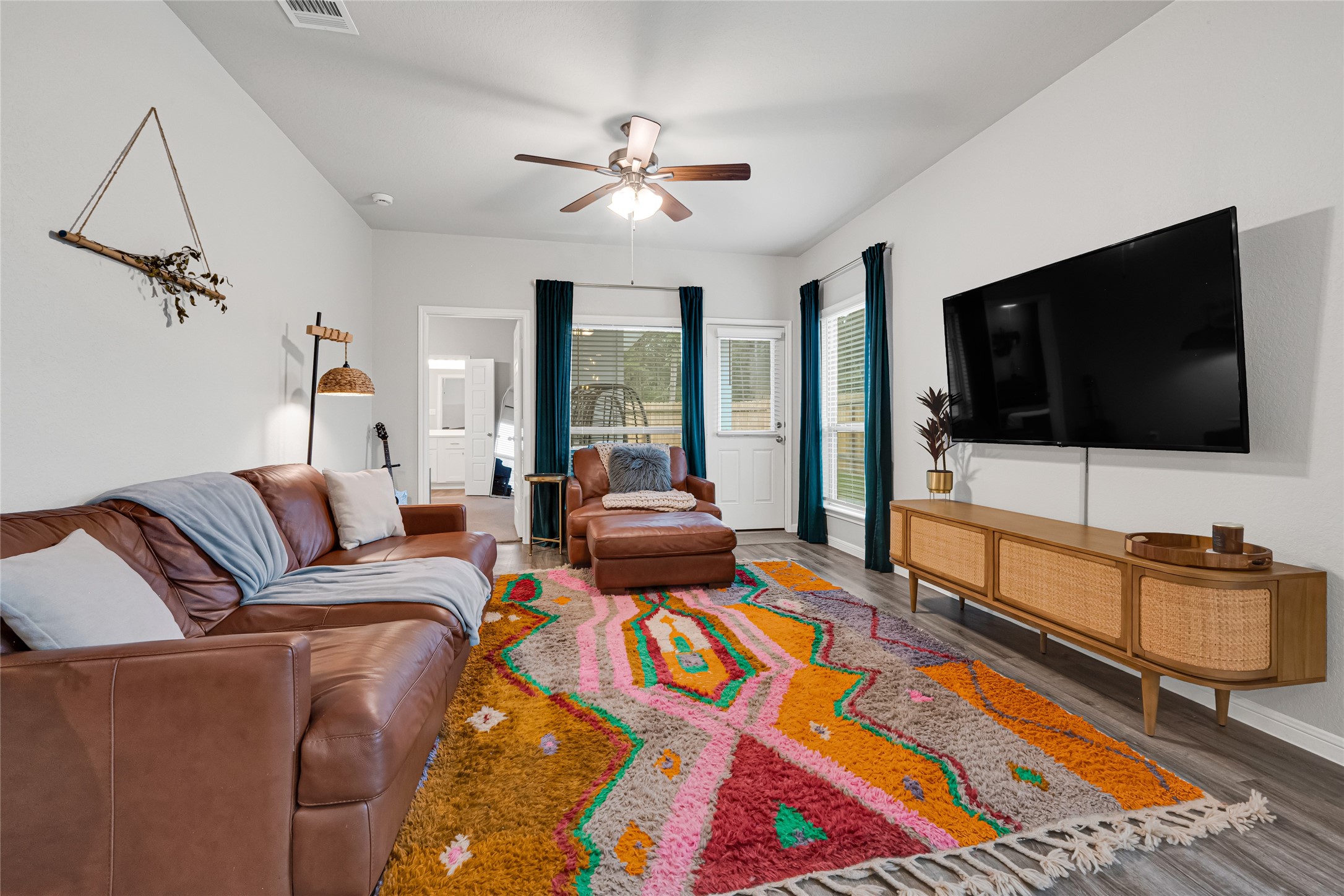 Cozy living room with a modern feel, featuring natural light streaming through large windows with designer curtains, and a decorative ceiling fan provides all the comforts you want to enjoy your living area.
