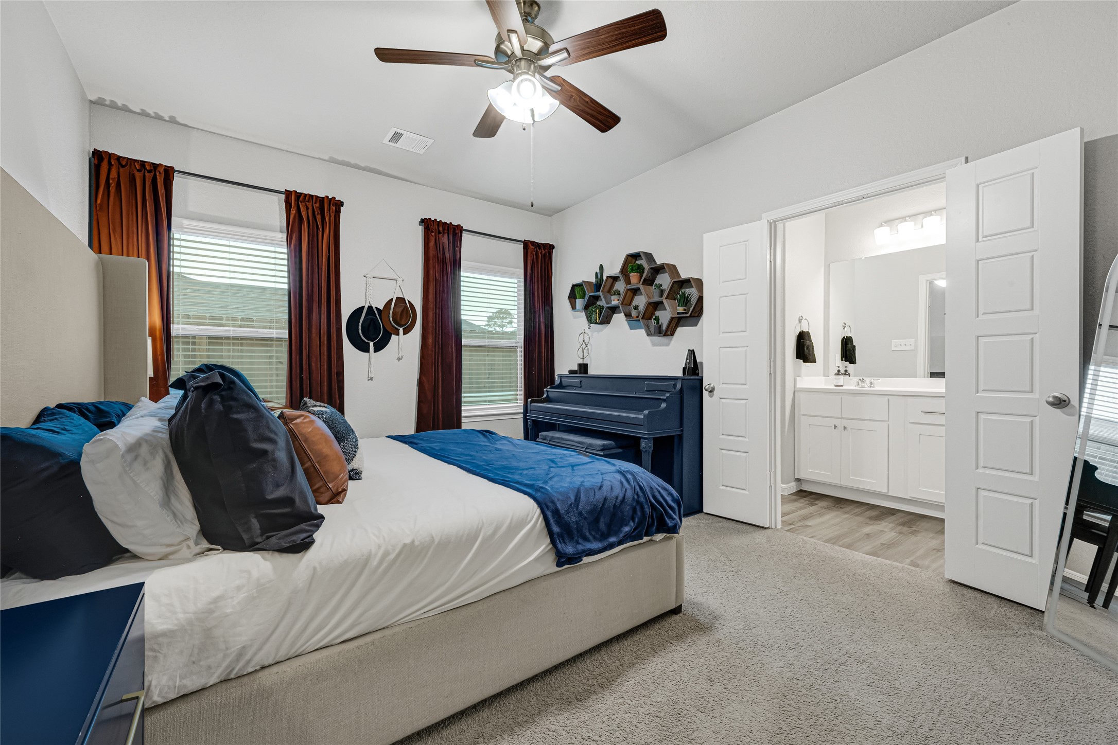 This perfectly sized bedroom features a neutral color palette with rich accents, the dark shade of the ceiling fan adds to the richness and over all feel of this cozy retreat.