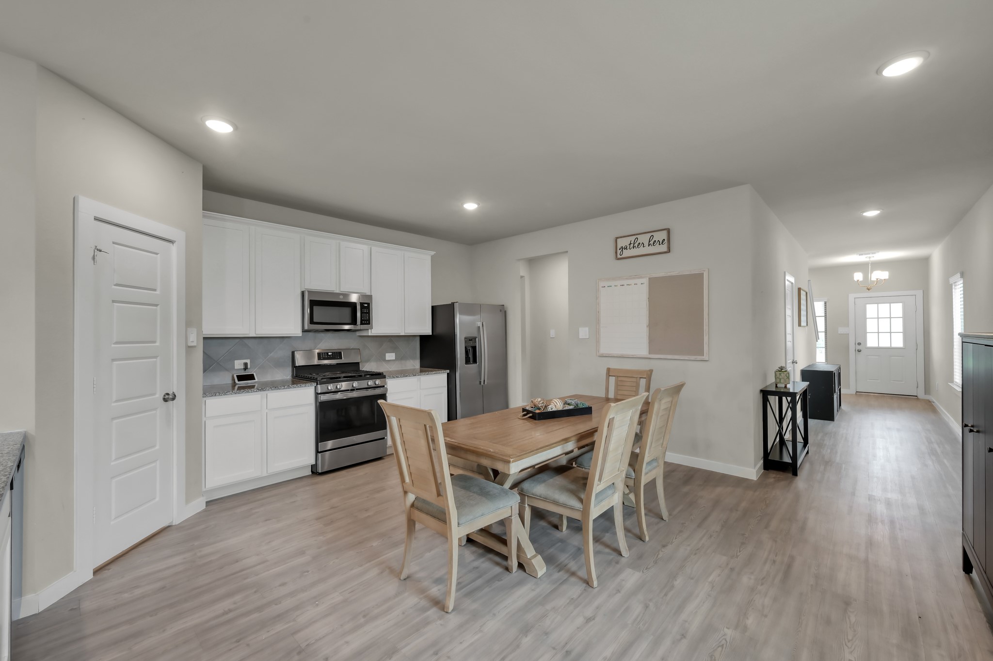This modern, open-concept kitchen and dining area with light wood flooring. The kitchen features white cabinetry, stainless steel appliances, and a sleek design. The dining space includes a wooden table with chairs, and the area is well-lit with recessed lighting, providing a warm and inviting atmosphere.