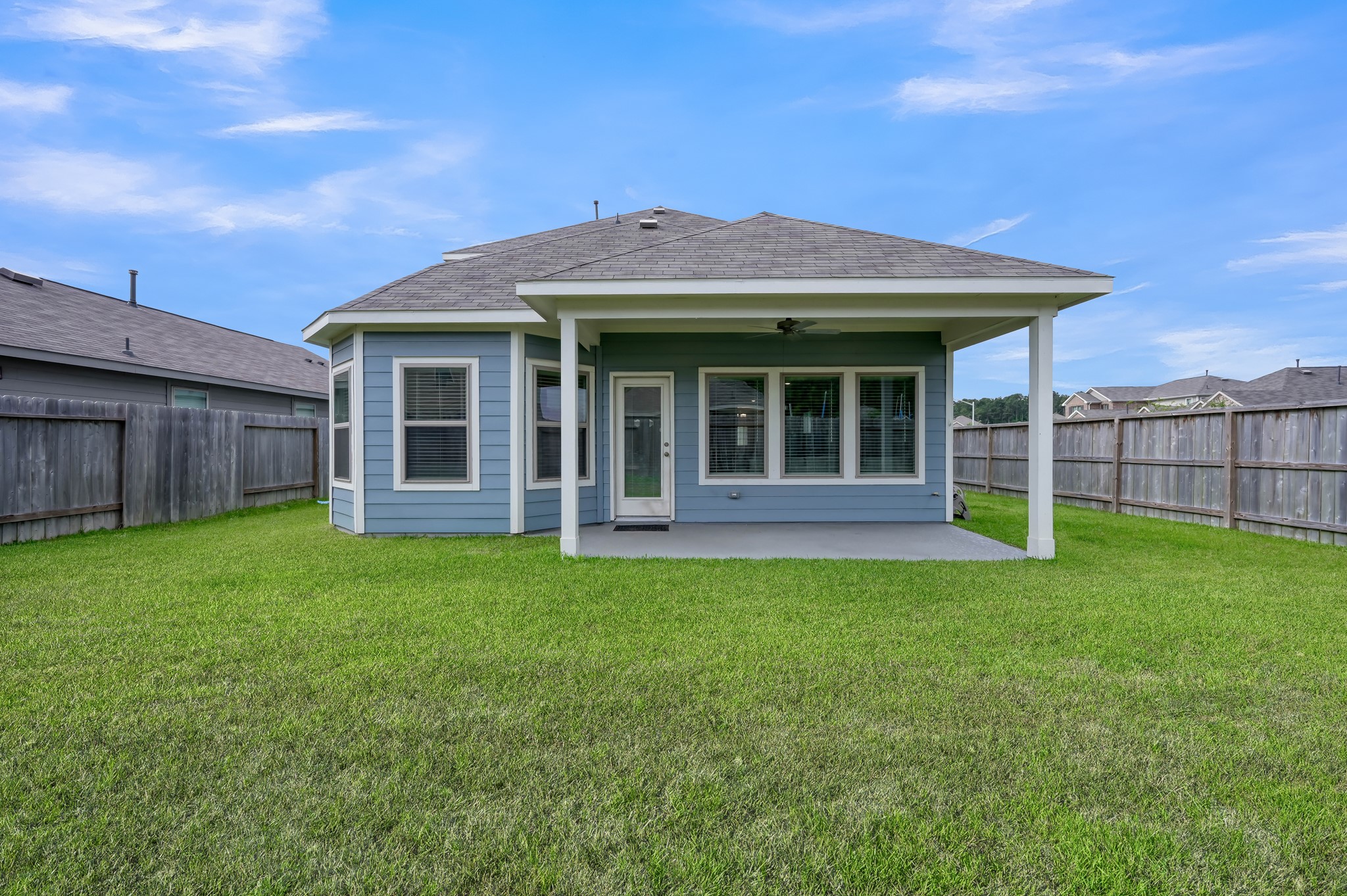 This photo shows a charming backyard with a covered patio, perfect for outdoor relaxation or entertaining. The house features a well-maintained lawn and a wooden fence providing privacy.