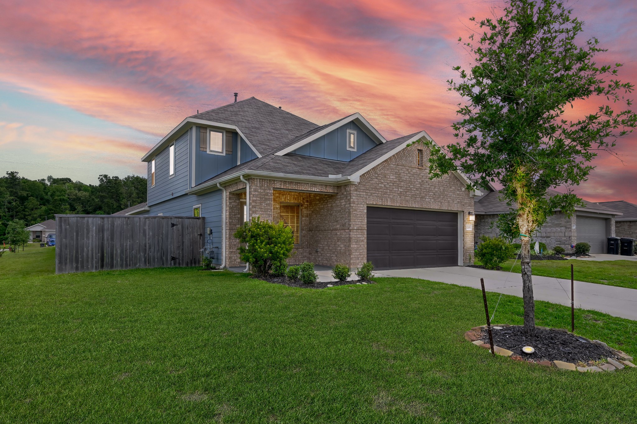 This charming two-story home features a modern design with a combination of brick and siding. It has a well-maintained front yard, a spacious driveway, and a two-car garage. The backdrop of a stunning sunset enhances its curb appeal.