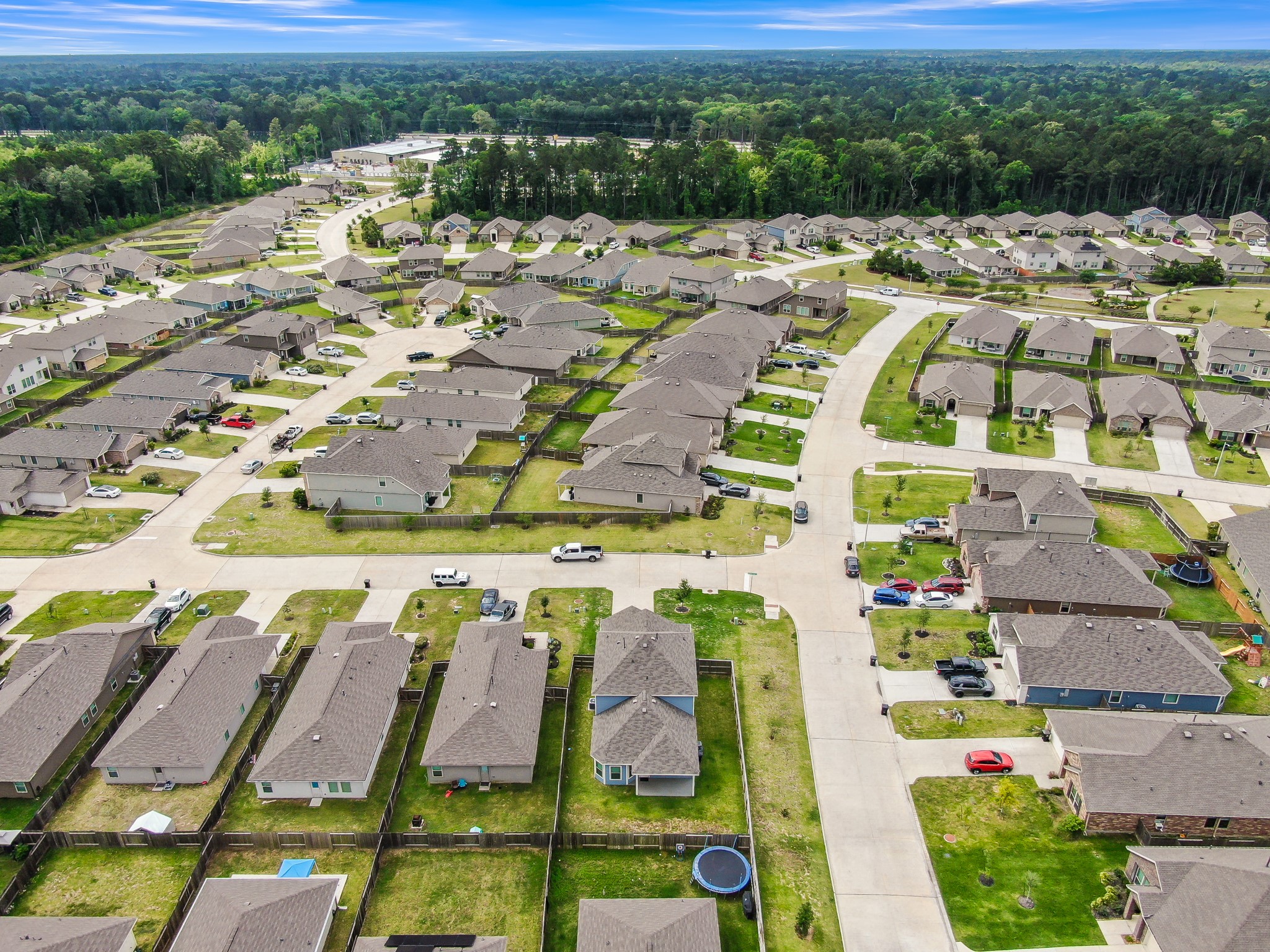 This aerial photo showcases a suburban neighborhood with neatly arranged single-family homes, well-maintained lawns, and a backdrop of lush greenery. The streets are wide and offer ample parking, creating a welcoming community atmosphere.