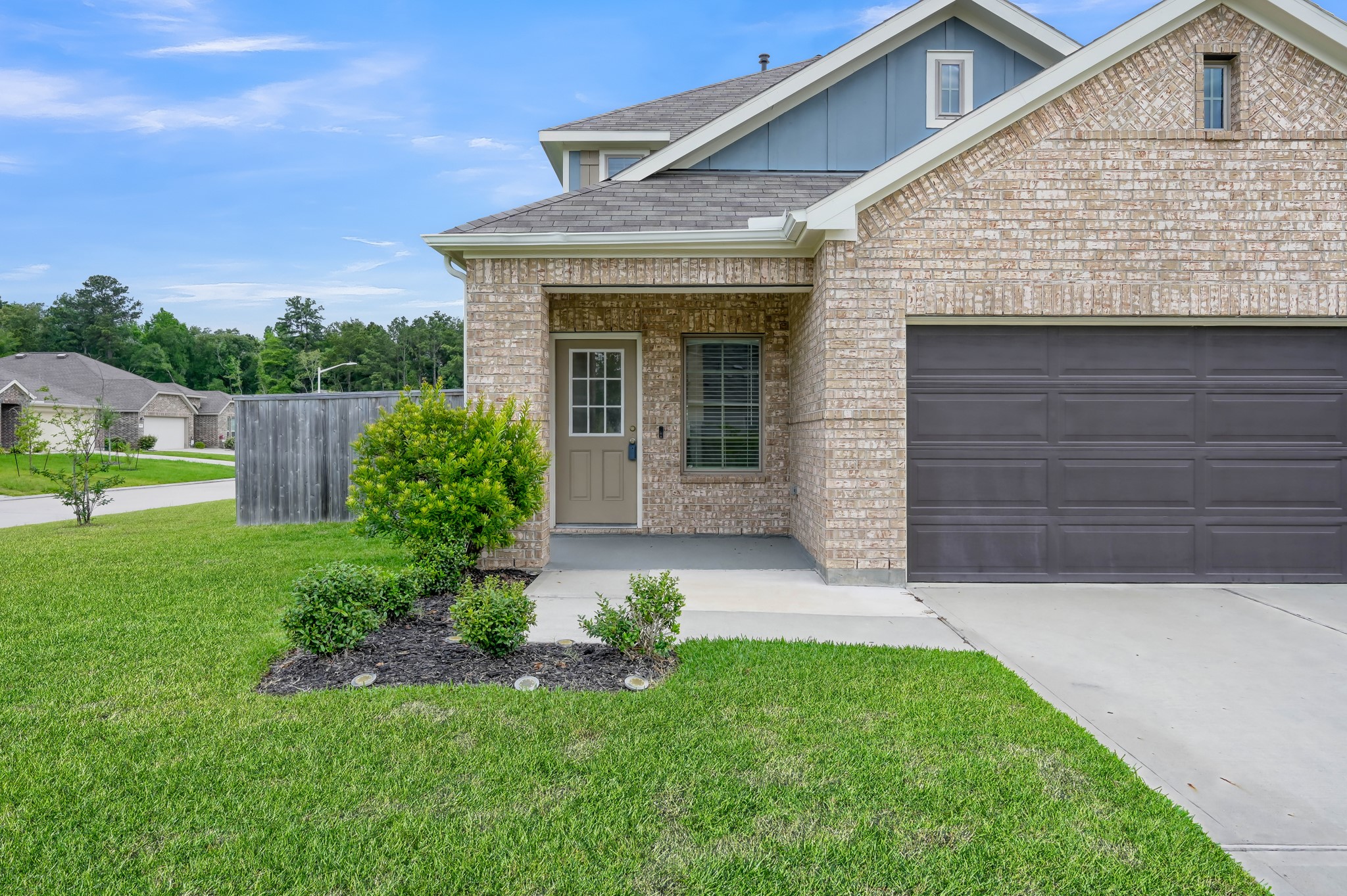 This is a modern brick home featuring a two-car garage and a small front porch. The exterior is well-maintained with a tidy lawn and landscaped shrubs, situated on a corner lot in a quiet neighborhood.