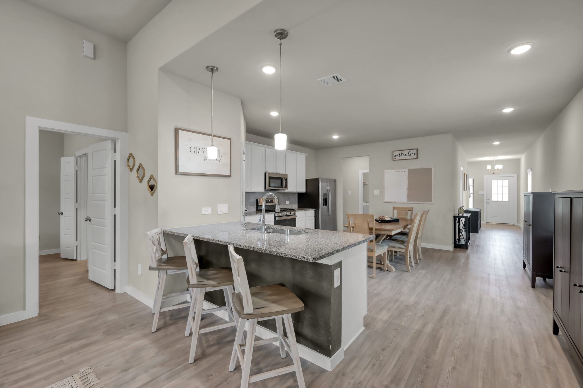 A modern, open-concept kitchen and dining area. It features a spacious kitchen island with bar seating, stainless steel appliances, and elegant pendant lighting. The room has a light, neutral color palette with hardwood floors, creating a welcoming and airy atmosphere.