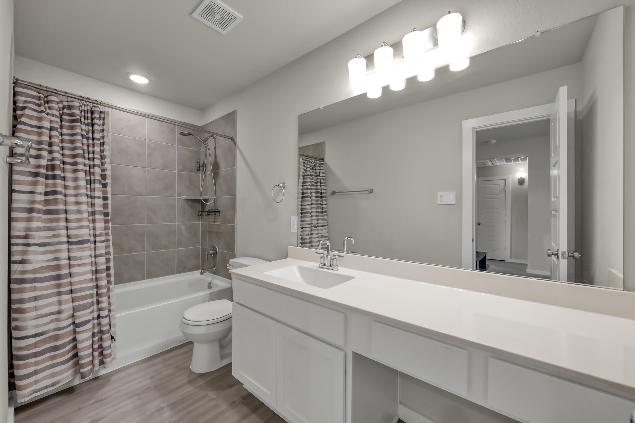 Modern bathroom featuring a large mirror, sleek vanity with ample counter space, and a full bathtub with a tiled shower area. Bright lighting and neutral tones create a clean, inviting atmosphere.