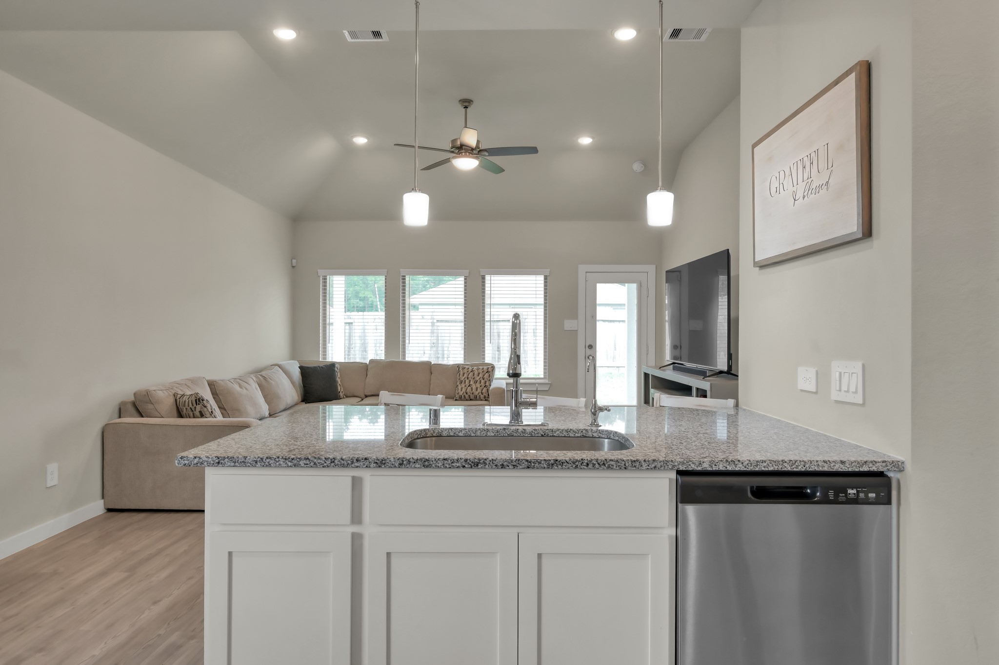 This spacious, open-concept living area features a modern kitchen with granite countertops and a central island, adjacent to a cozy living room with large windows and a ceiling fan.