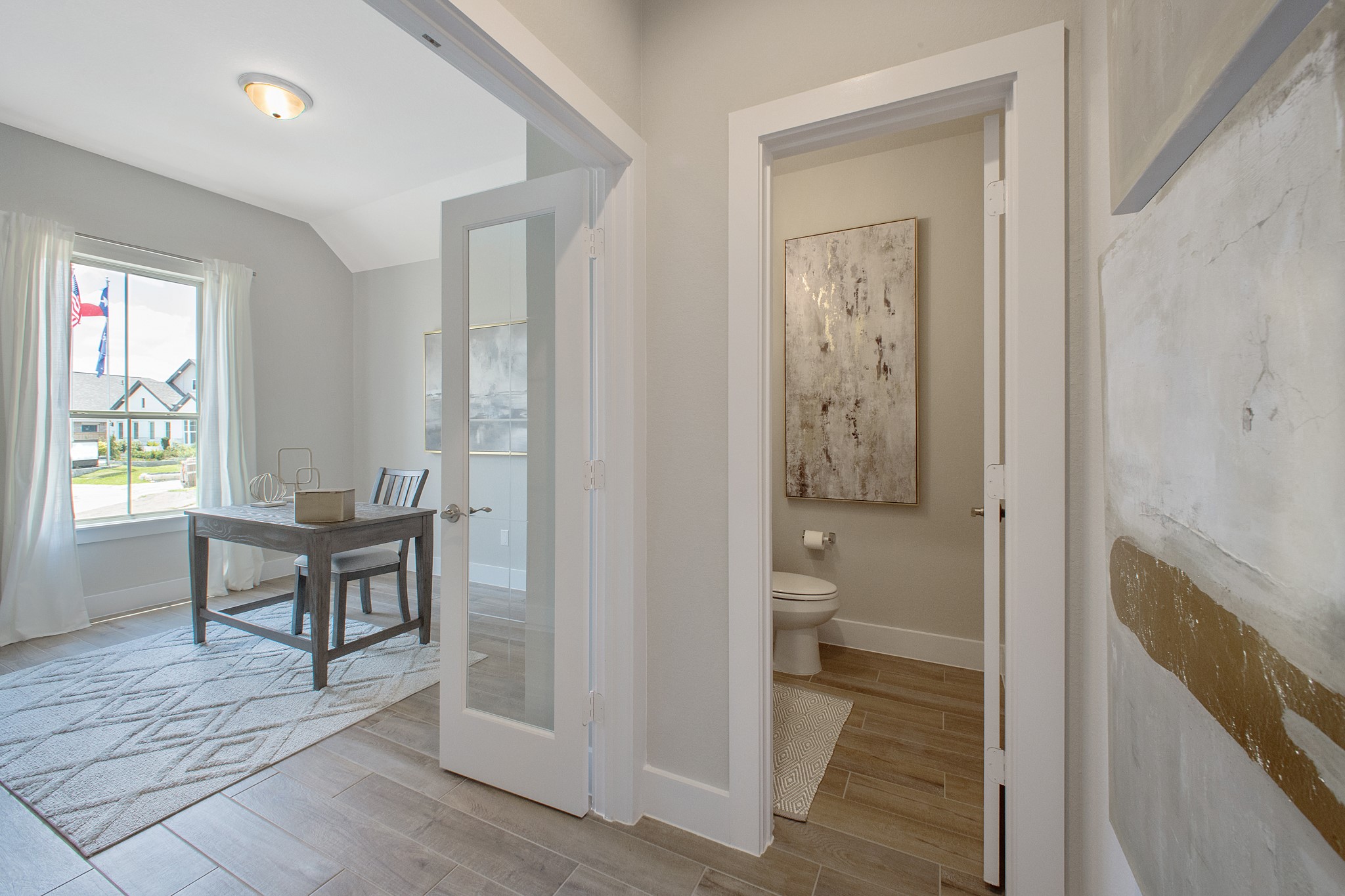 Experience the perfect blend of sophistication and warmth in this home office, boasting elegant wood-look tile flooring and flooded with natural light from expansive windows and French doors.