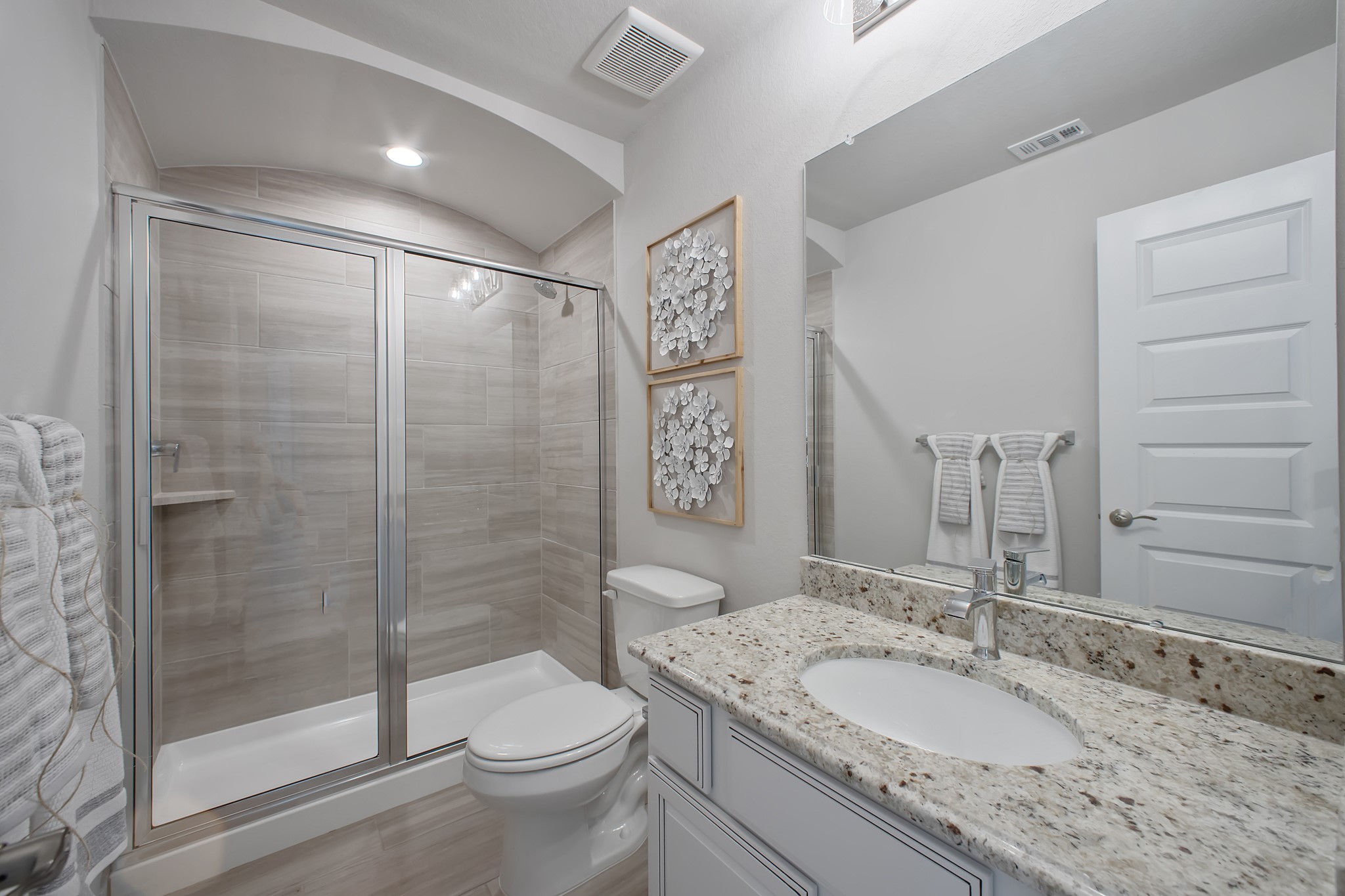 Secondary bath features tile flooring, walk-in shower with tile surround, light stained wood cabinets, beautiful light countertop.