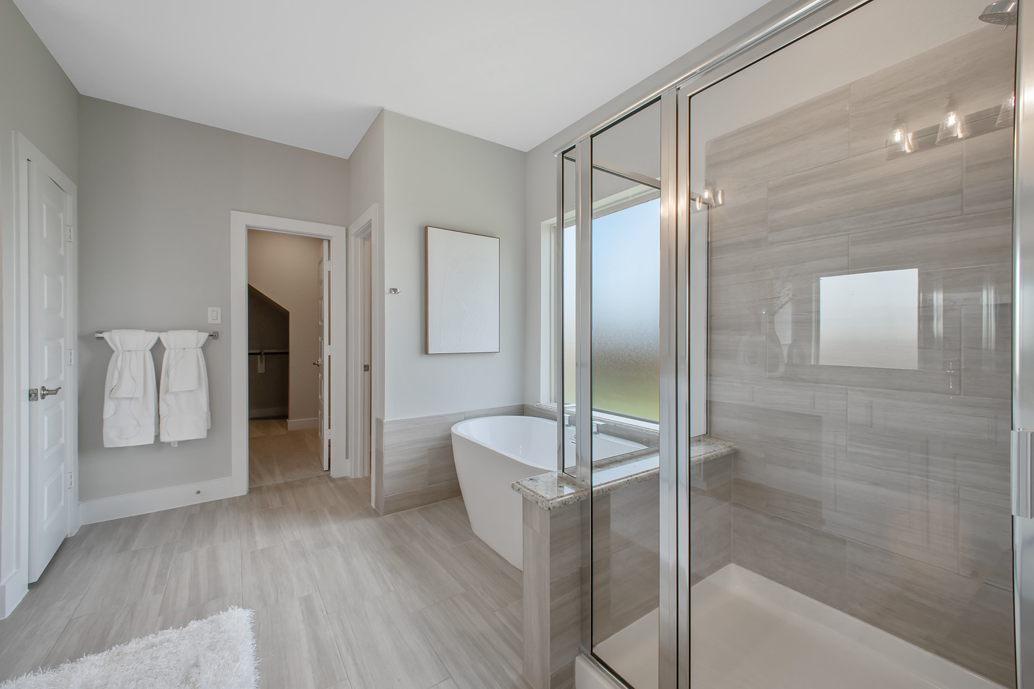 Escape to a spa-like oasis in this primary bathroom. Enjoy a walk-in shower with tile surround, a separate garden tub with custom detailing, and an elegant vanity featuring light countertops, modern hardware, and beautiful vanity lights. Experience luxury and relaxation in every detail.