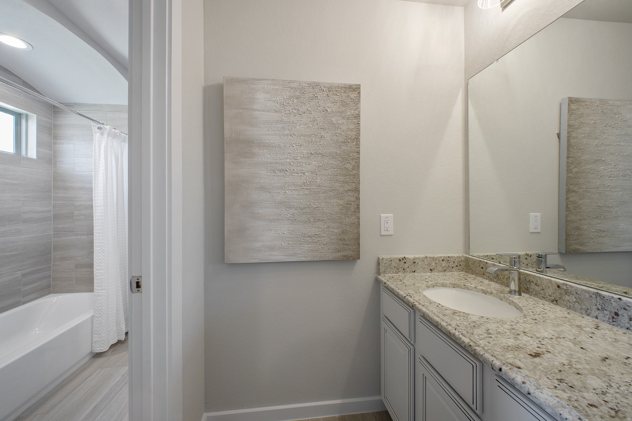Secondary bath features tile flooring, bath/shower combo with tile surround, light stained wood cabinets, beautiful light countertop.