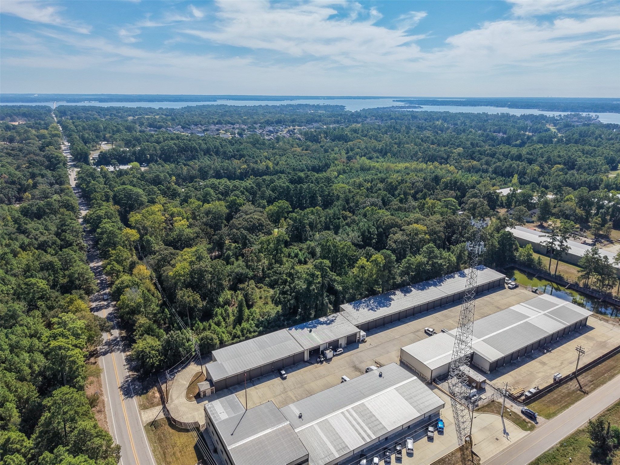 Wide-angle aerial showcasing the heavily wooded surroundings, nearby roadway, and expansive views toward Lake Conroe. An excellent perspective of the property's location within the growing Lake Conroe area.