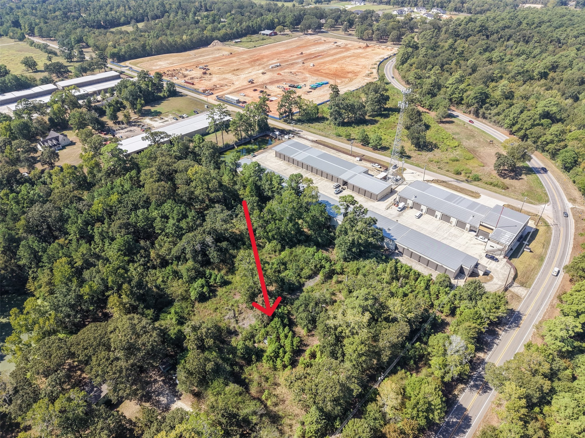 Expansive aerial view capturing the property's wooded terrain, surrounding roadways, and nearby commercial development. A desirable location offering potential for a variety of future uses.