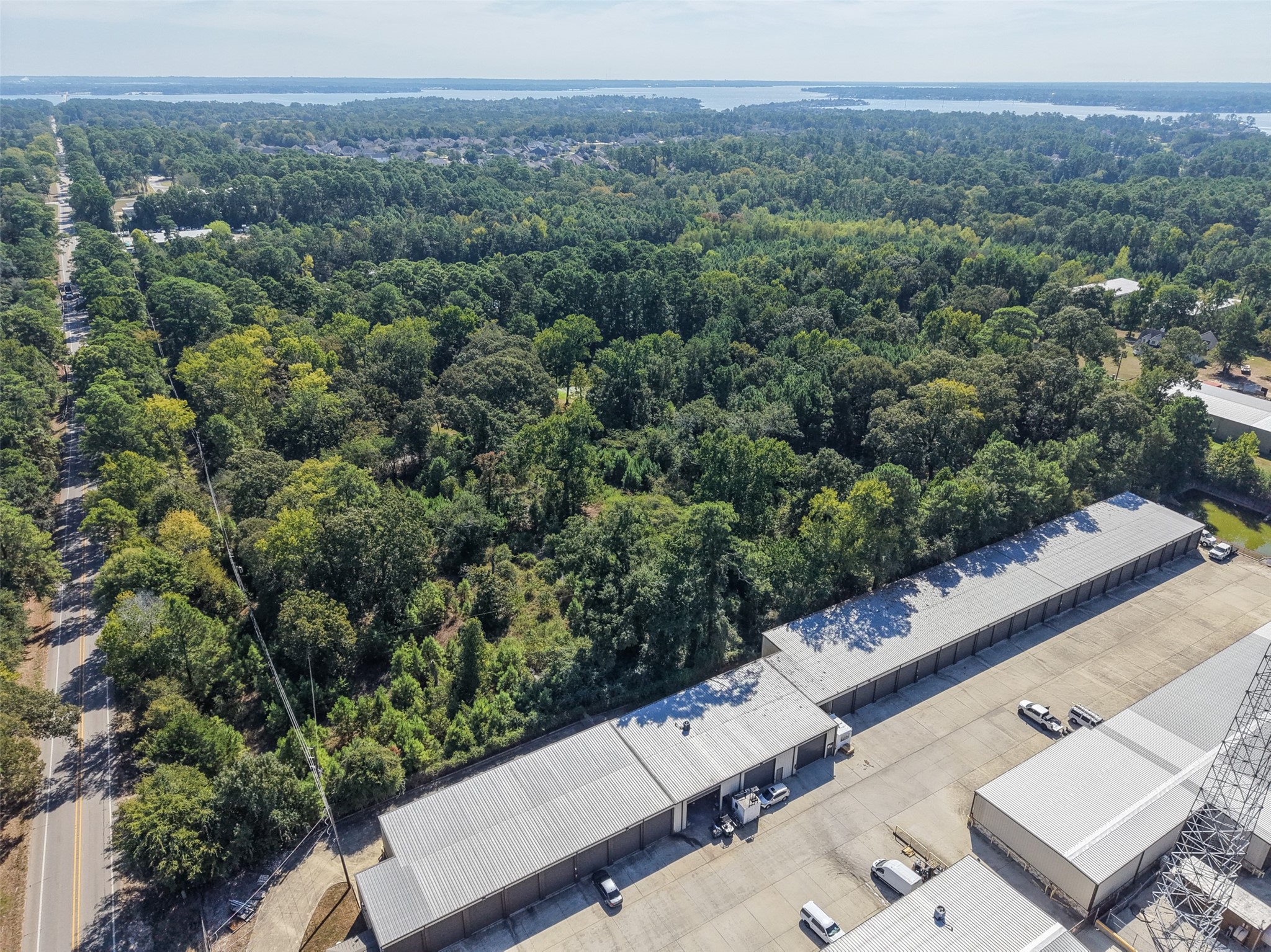 Wide-angle aerial showcasing the heavily wooded surroundings, nearby roadway, and expansive views toward Lake Conroe. An excellent perspective of the property's location within the growing Lake Conroe area.