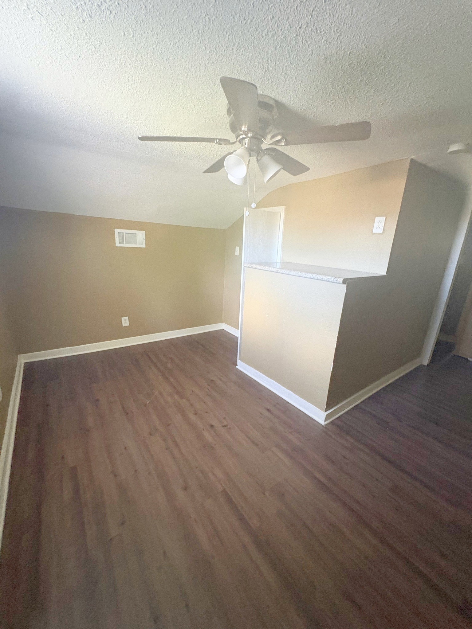 The upper-level area has wood-look flooring, a ceiling fan, and a half wall by the stairs.
