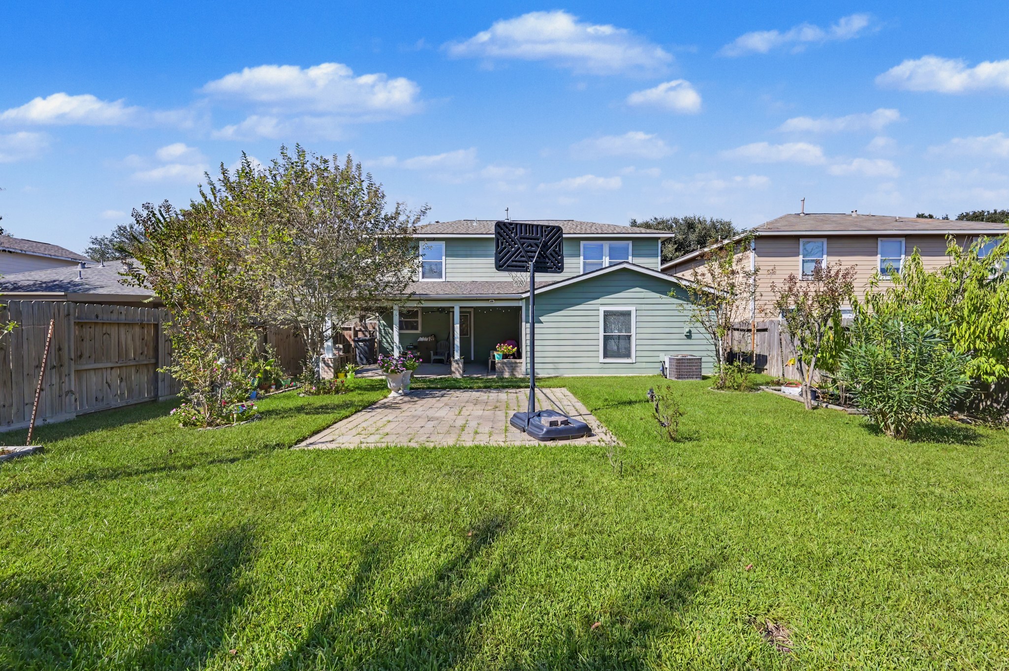 Spacious backyard featuring lush green lawn, mature trees, and a paved patio area perfect for outdoor activities and relaxation.