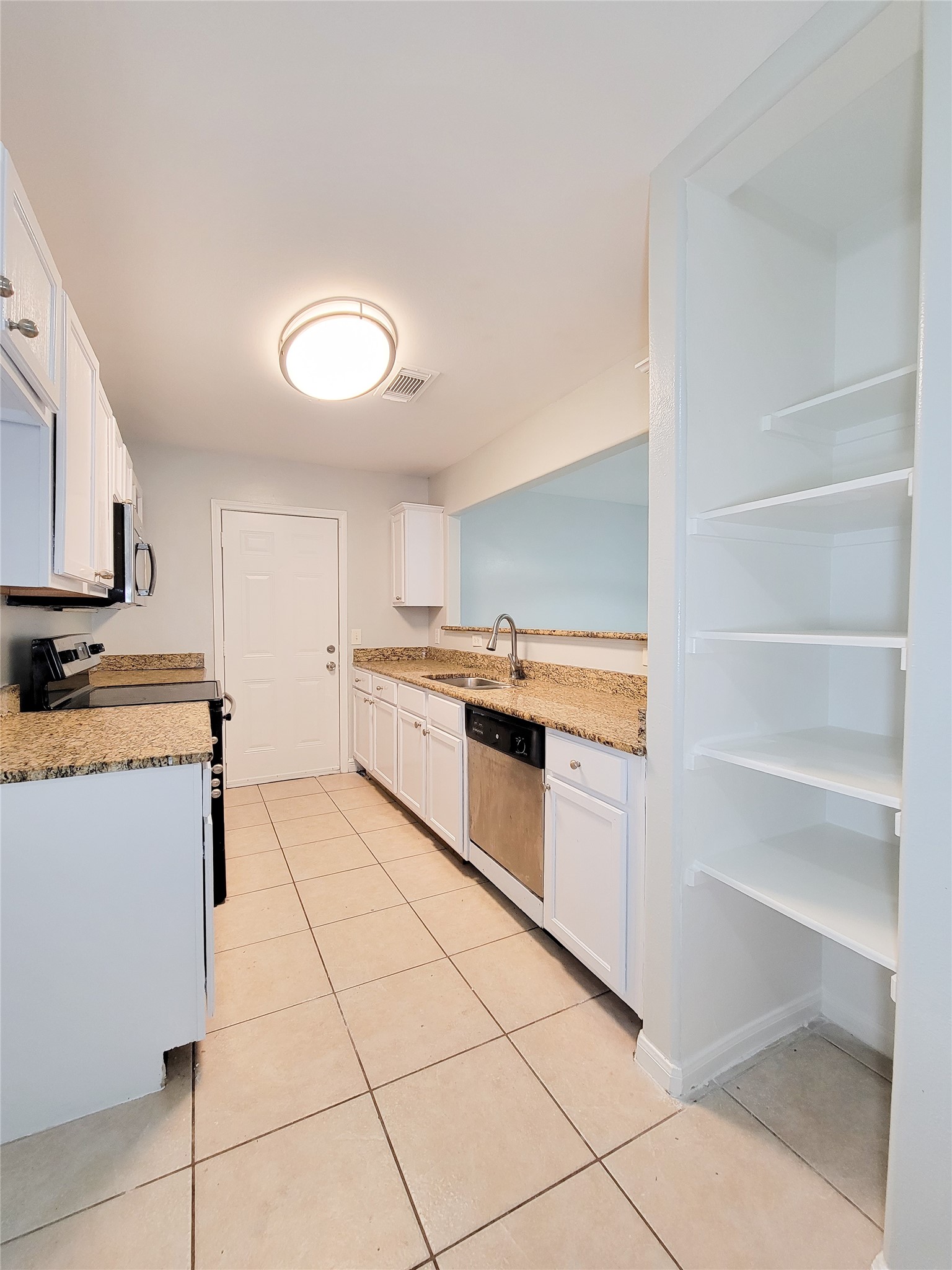 Bright kitchen featuring granite countertops, stainless steel appliances, and ample storage with open shelving and white cabinetry.