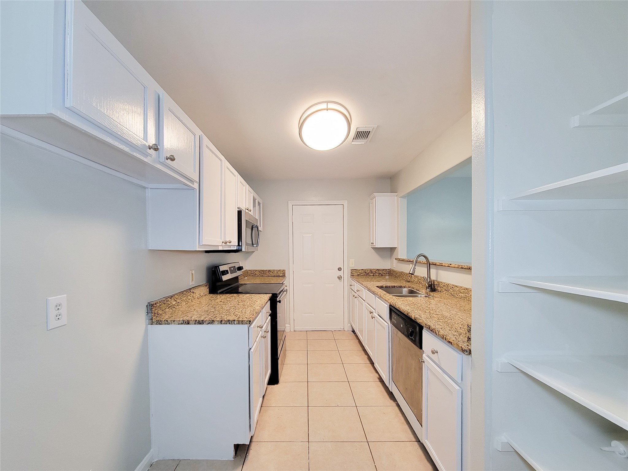 Bright galley kitchen featuring granite countertops, stainless steel appliances, and ample cabinet storage, complemented by a convenient open shelving unit.